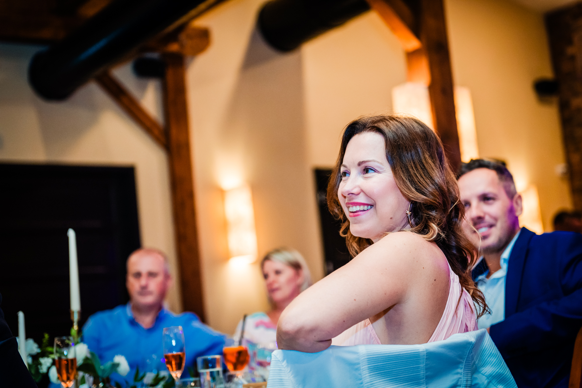 Wedding guest smiles during speeches inside the warmly lit reception room at Dunai Csónakház.