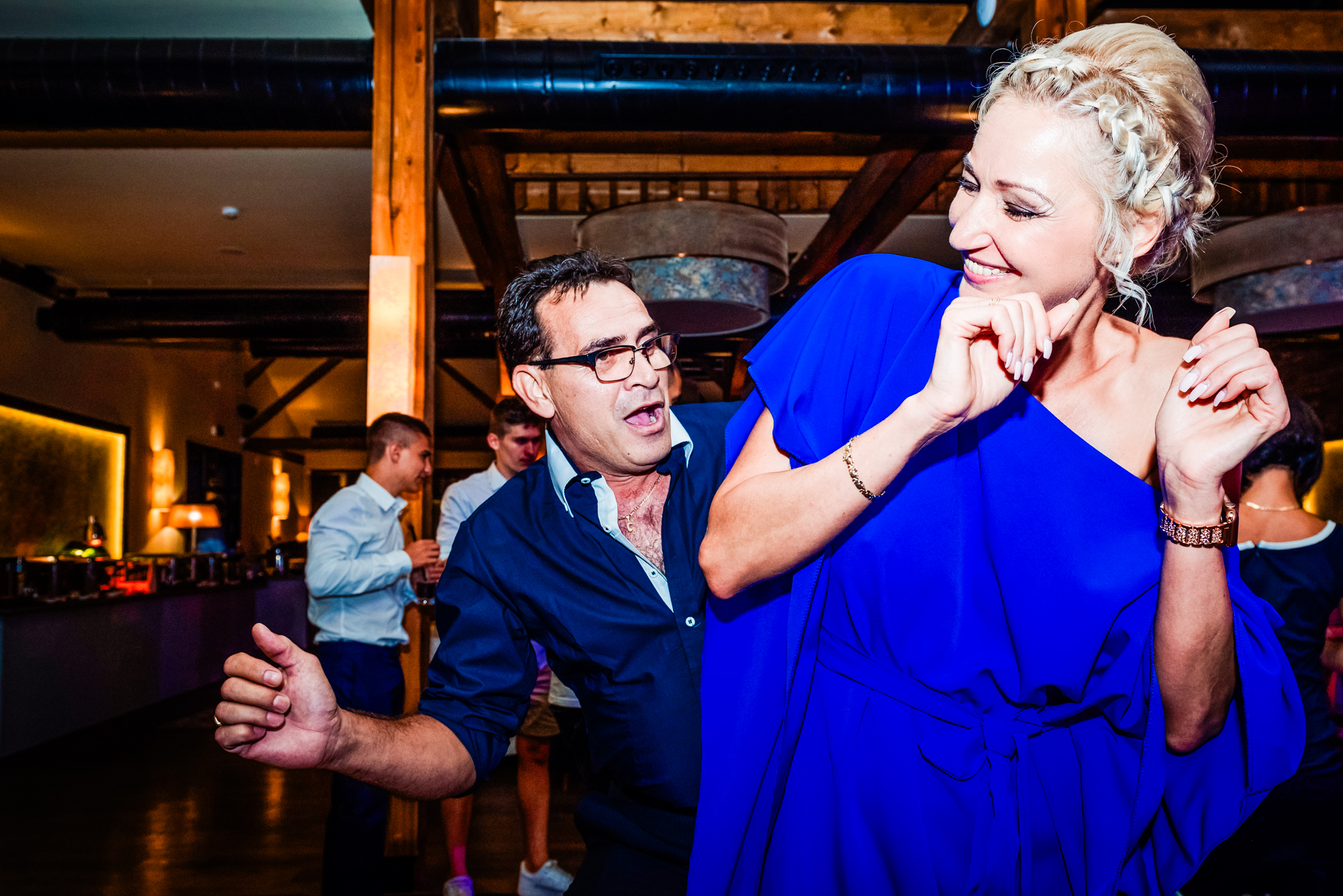 Wedding guests laugh and dance together under colourful reception lighting.