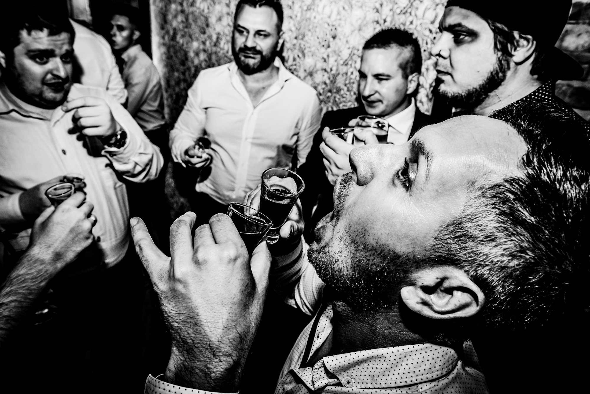 Wedding guests gather for a late-night toast with shots and lively conversation.