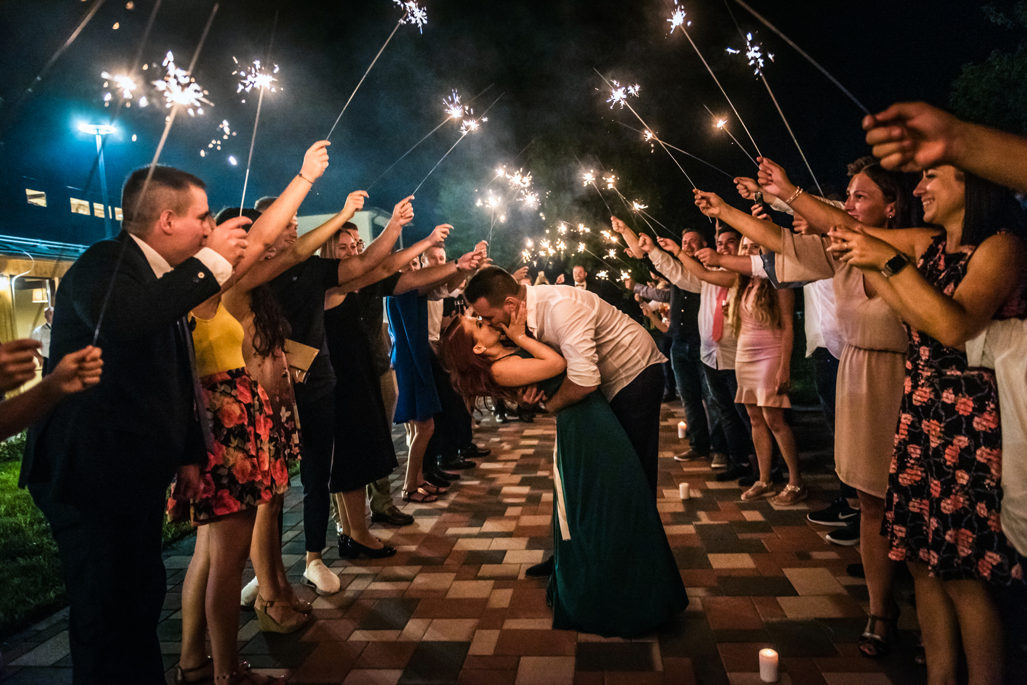 Newlyweds share a kiss beneath a sparkler tunnel created by wedding guests.