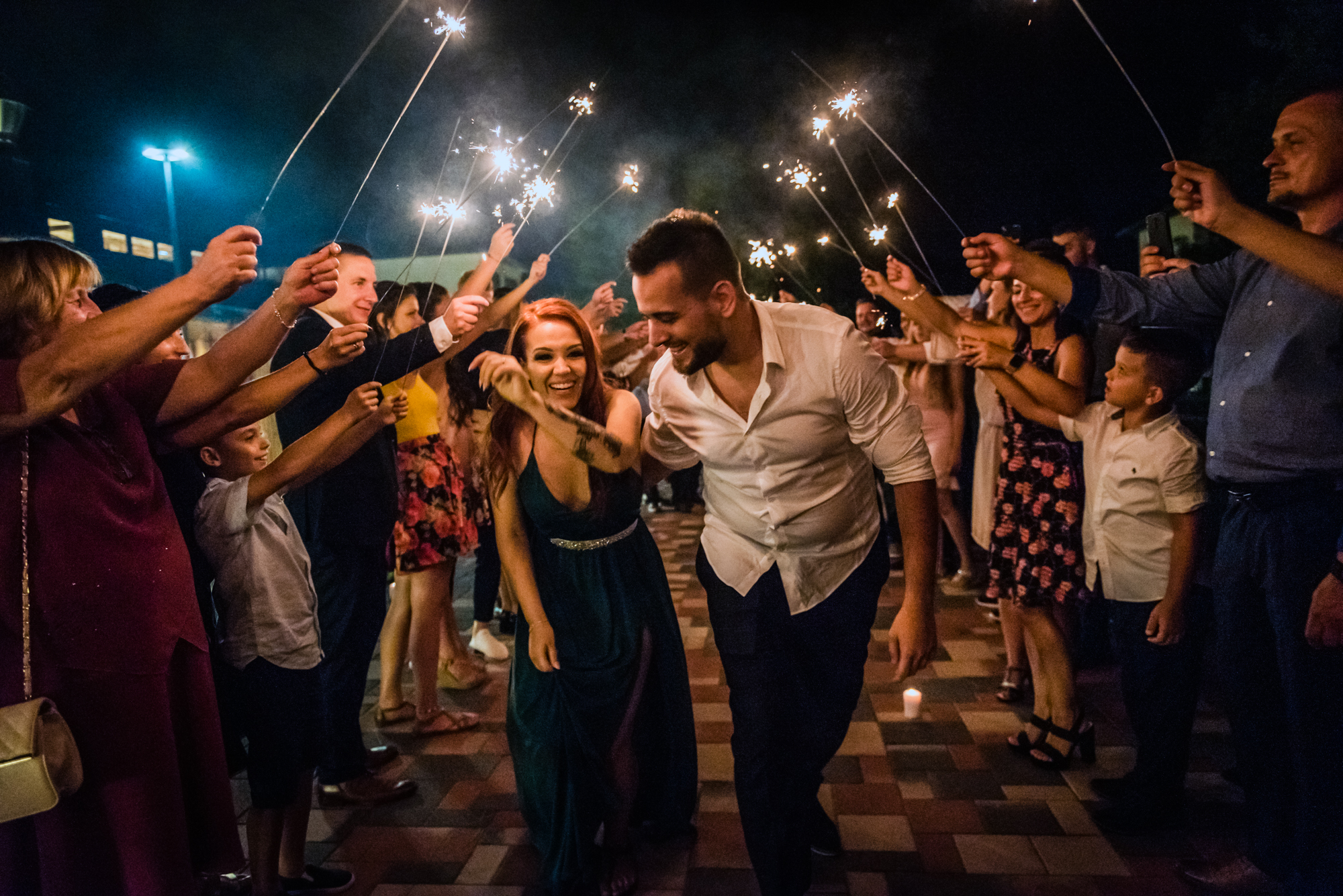 Bride and groom leave through a sparkler exit surrounded by cheering family and friends.