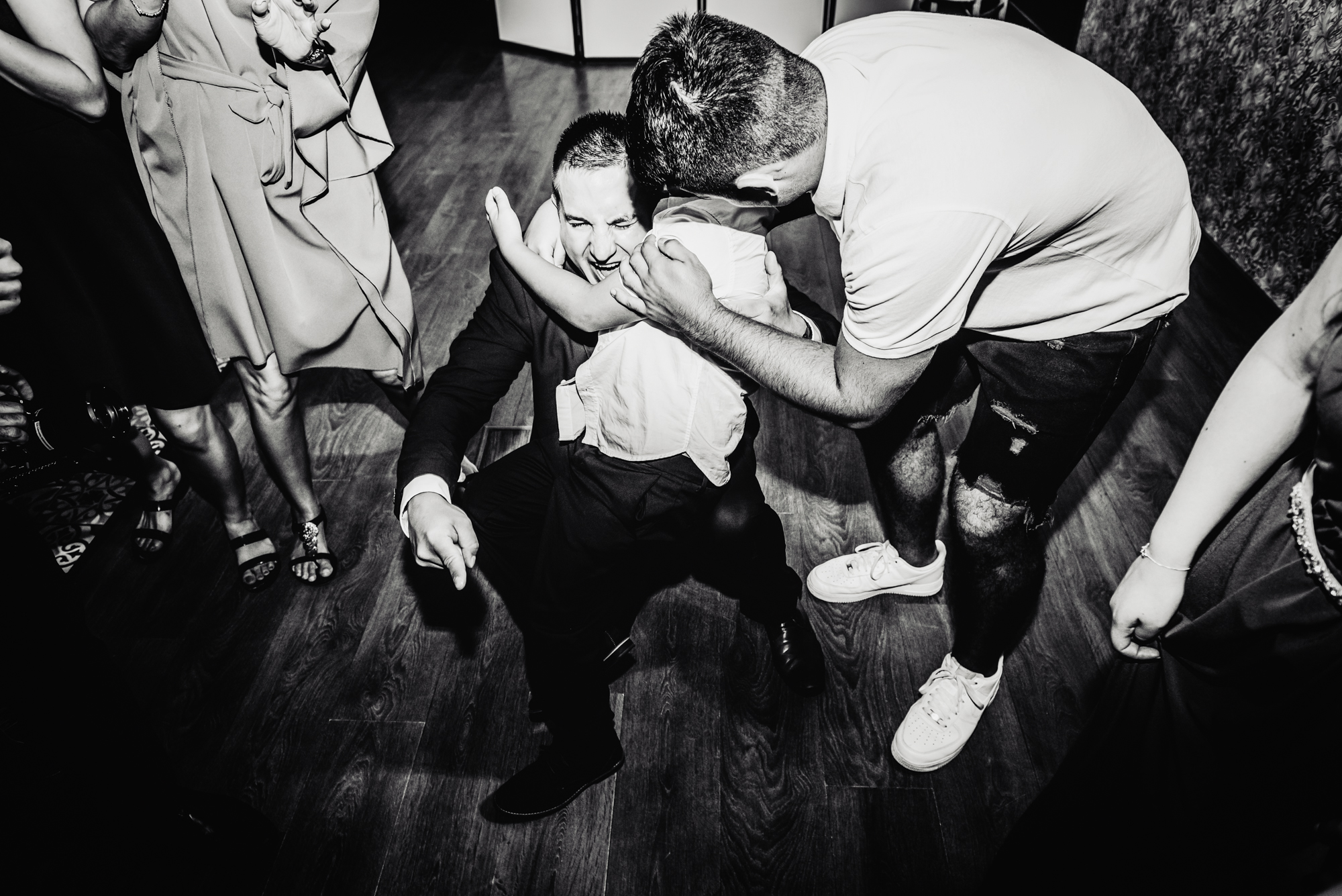 Child hugs a kneeling wedding guest while others laugh on the dance floor.