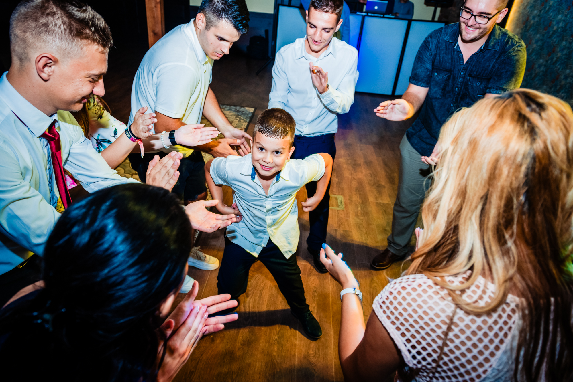 A young boy dances on the dancefloor surrounded by wedding guests.