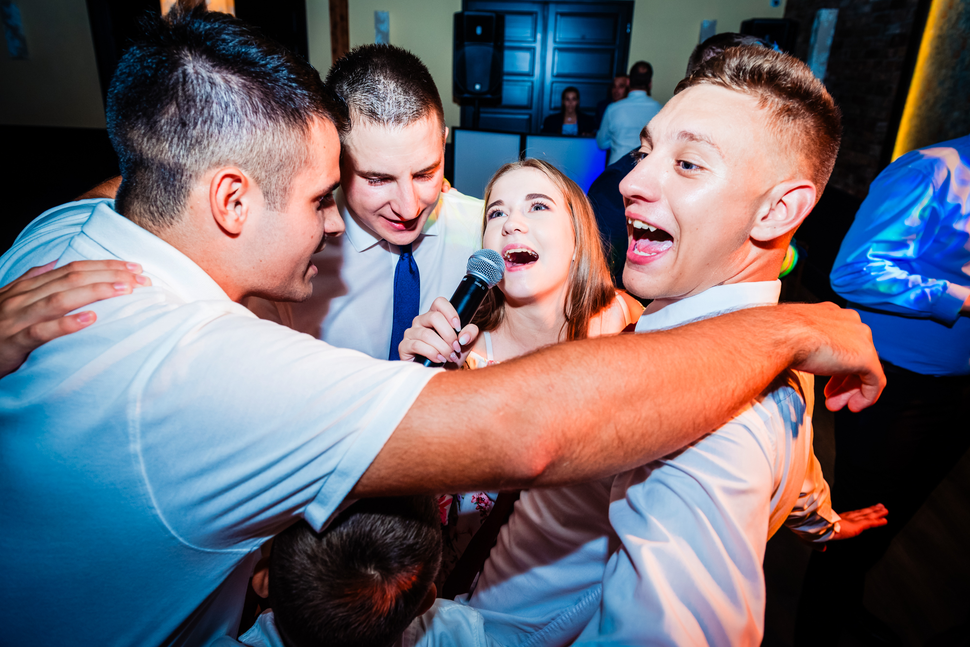 Wedding guests sing together around a microphone during the lively evening reception.