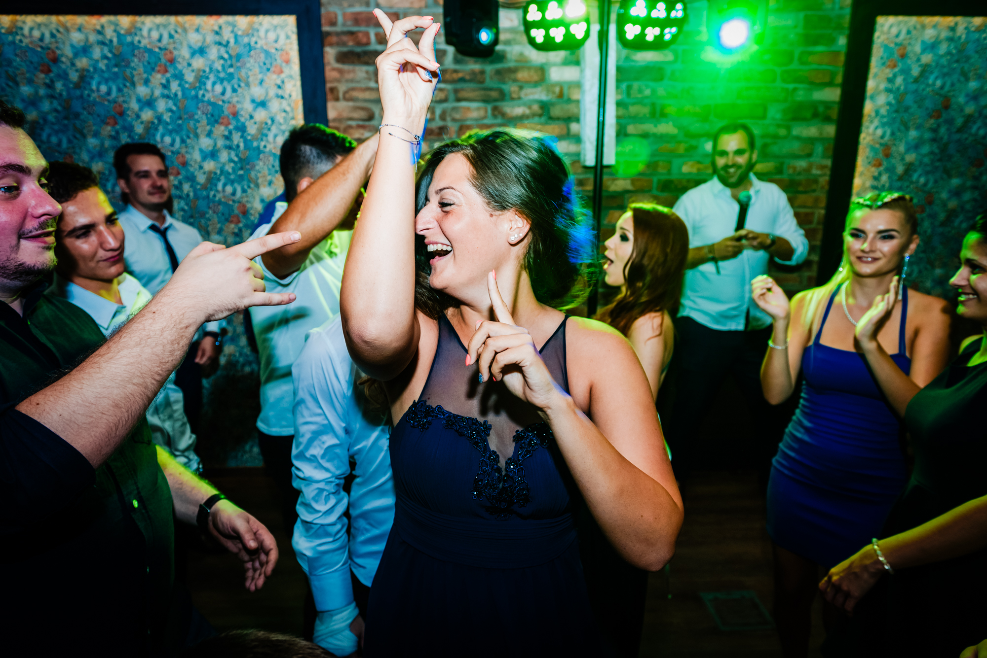 Wedding guest laughs while dancing beneath green party lights surrounded by friends on the dance floor.