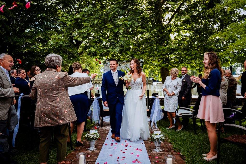 Newly married couple walking back down aisle surrounded by guests after outdoor wedding ceremony.