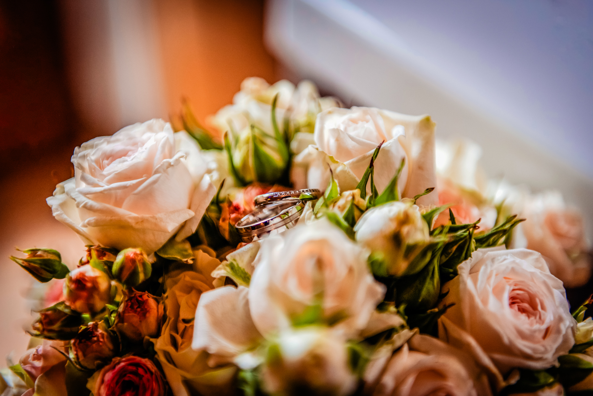 Wedding rings resting inside a bouquet of blush and ivory roses during bridal preparations.