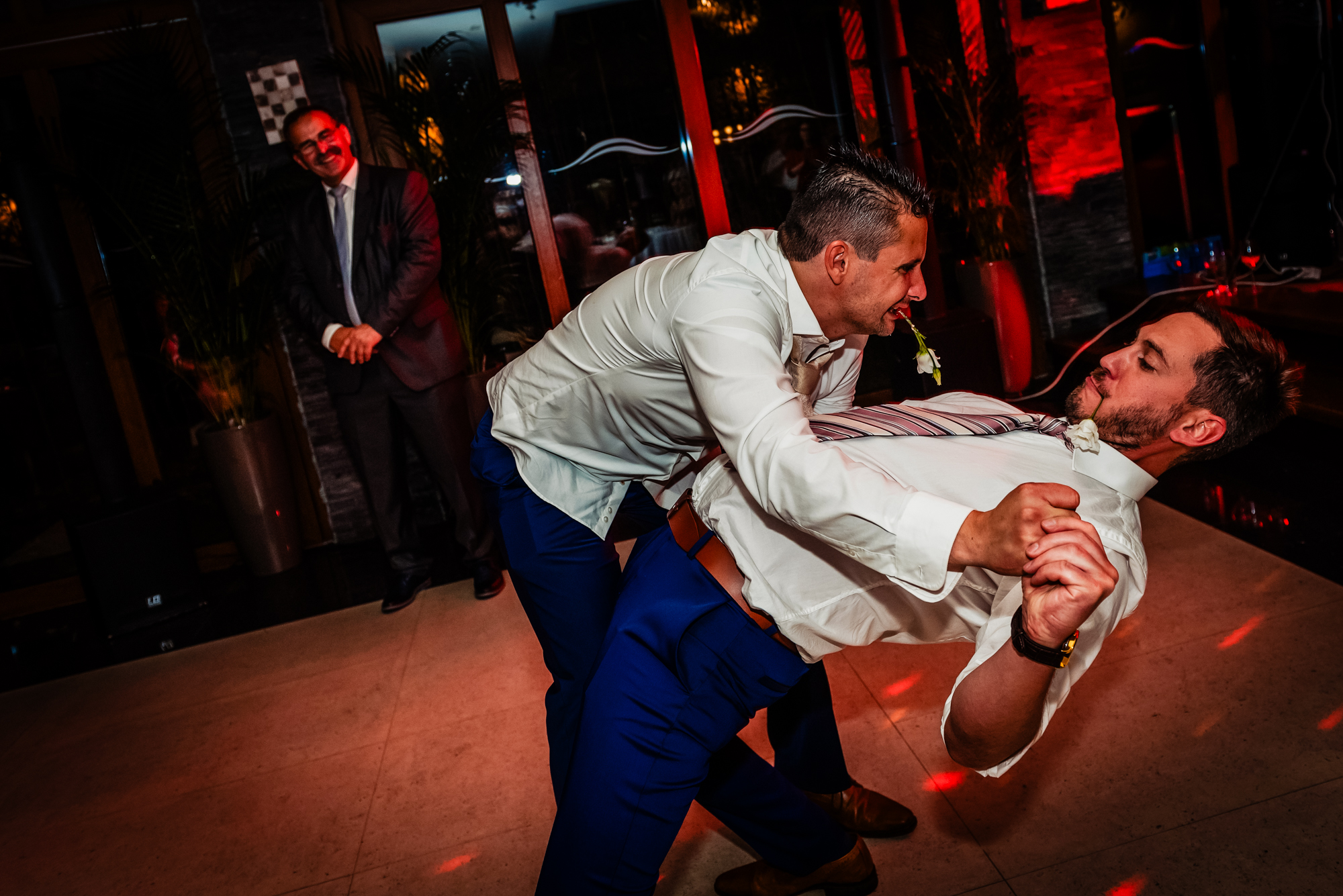 Groom dipping groomsman onto dance floor during lively wedding party at Duna Garden Hotel.