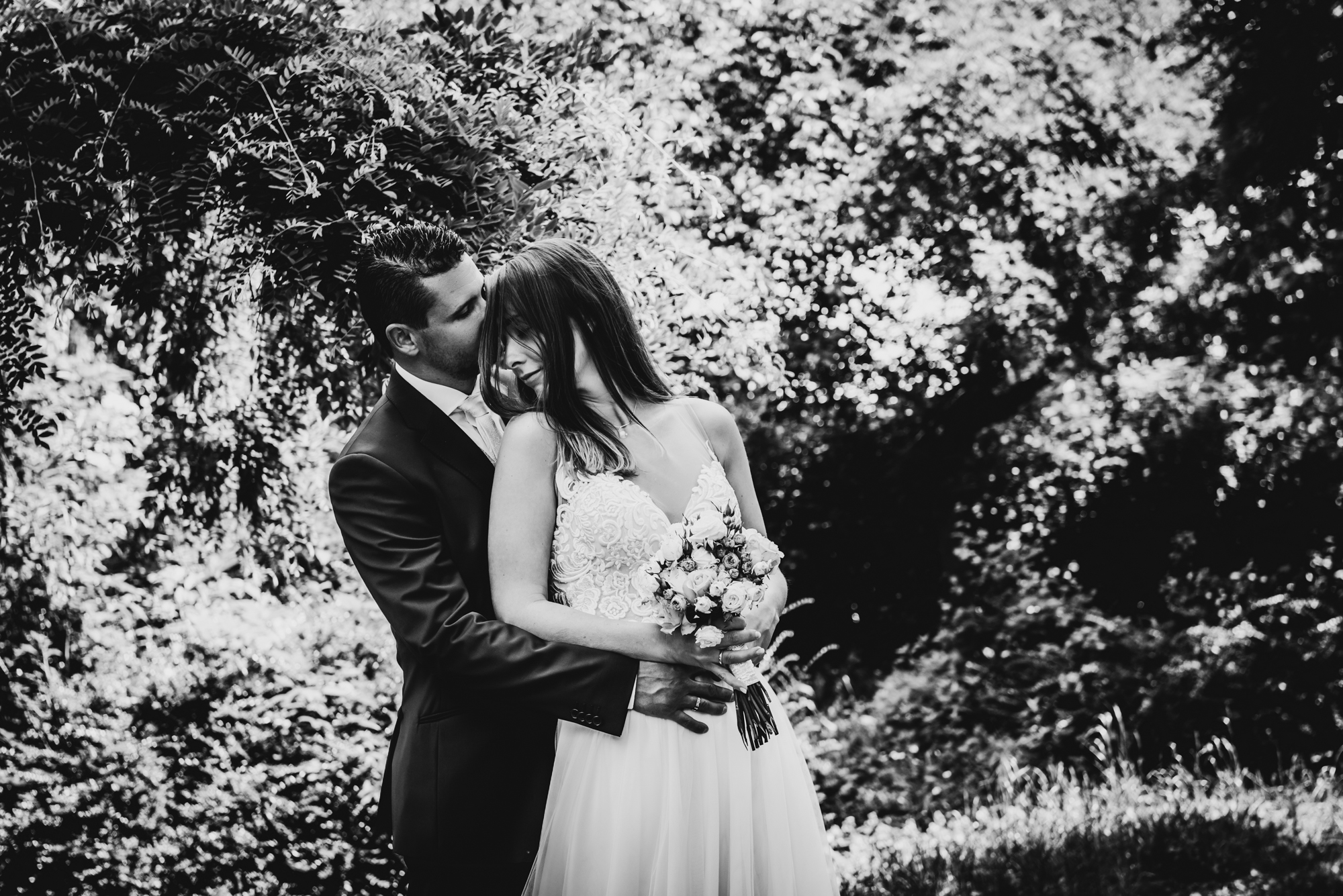 Bride and groom embracing in garden portrait surrounded by soft summer light and trees.