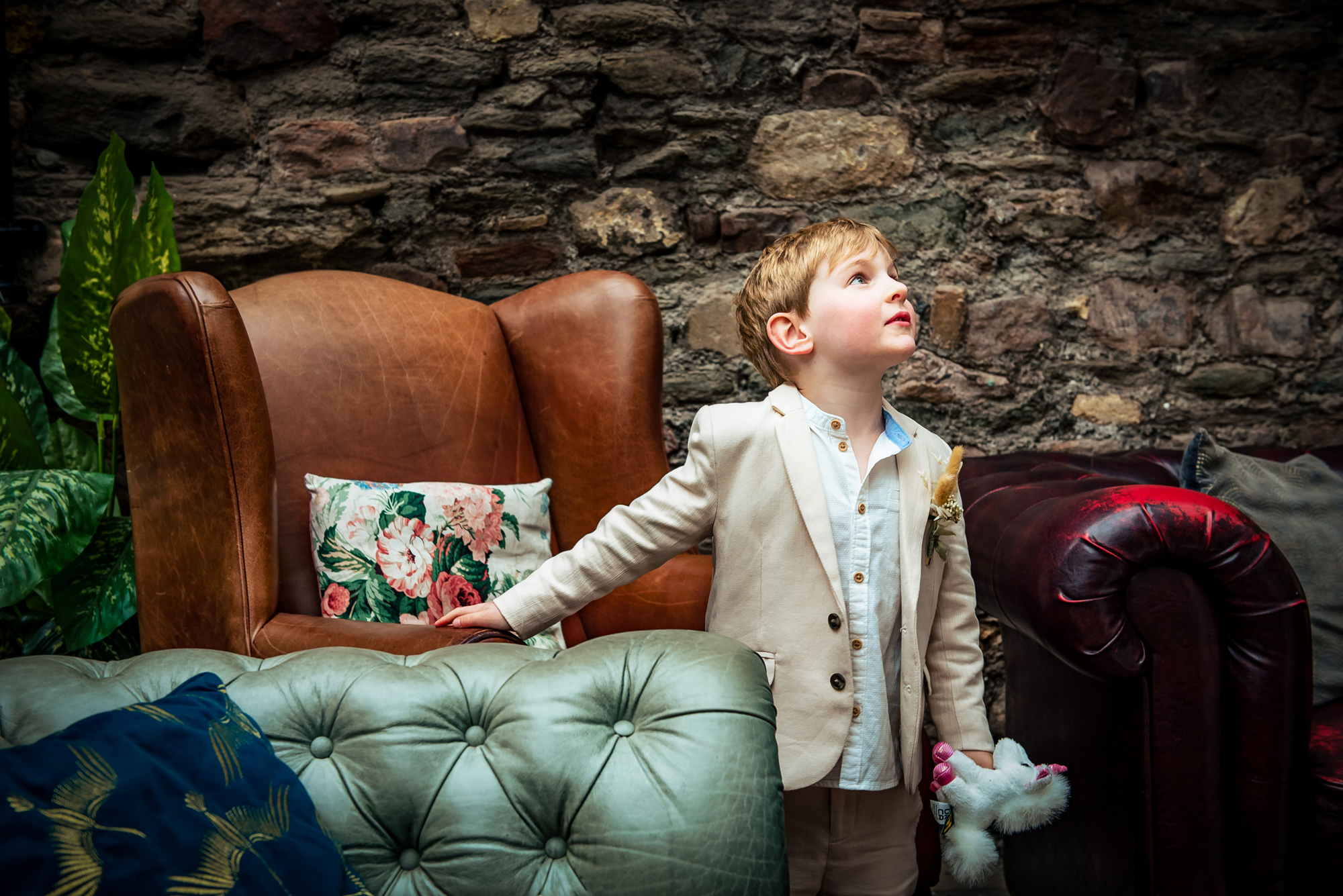 Young boy standing beside vintage armchair holding toy in relaxed reception space.