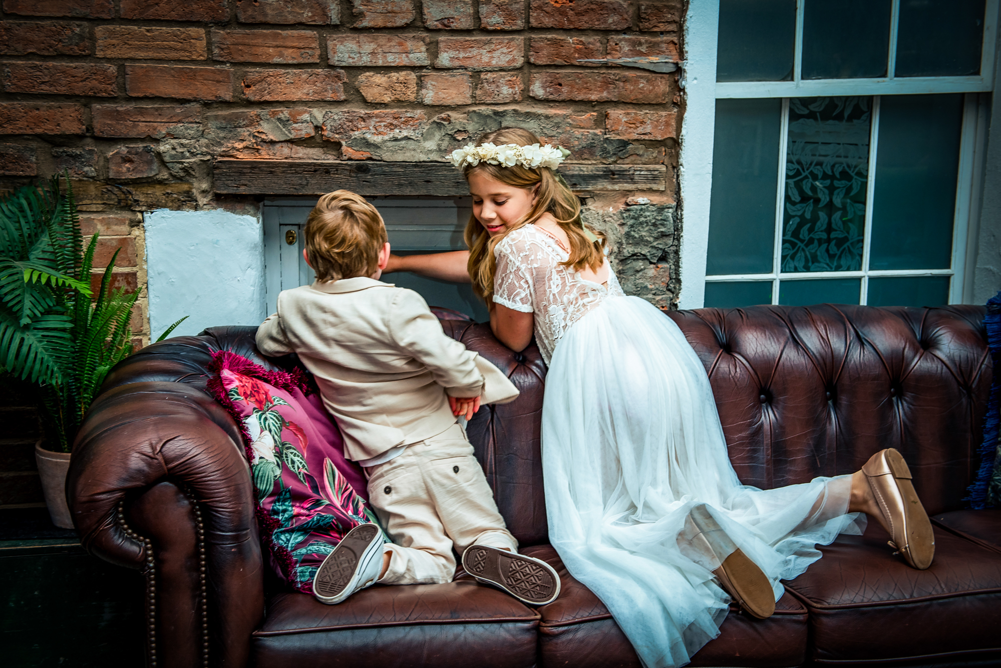 Children leaning over leather sofa by brick wall at Radnor Rooms Bristol wedding.