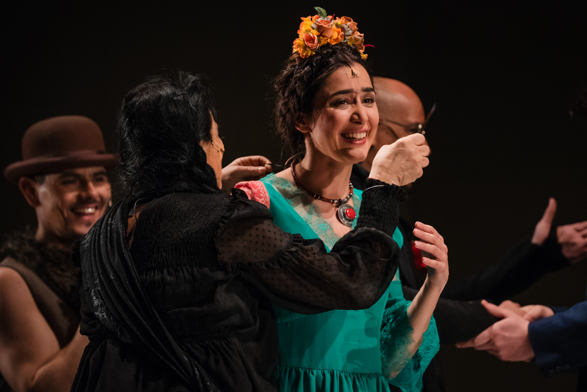 Actress in green dress smiles during emotional ensemble moment in Frida Kahlo theatre production.