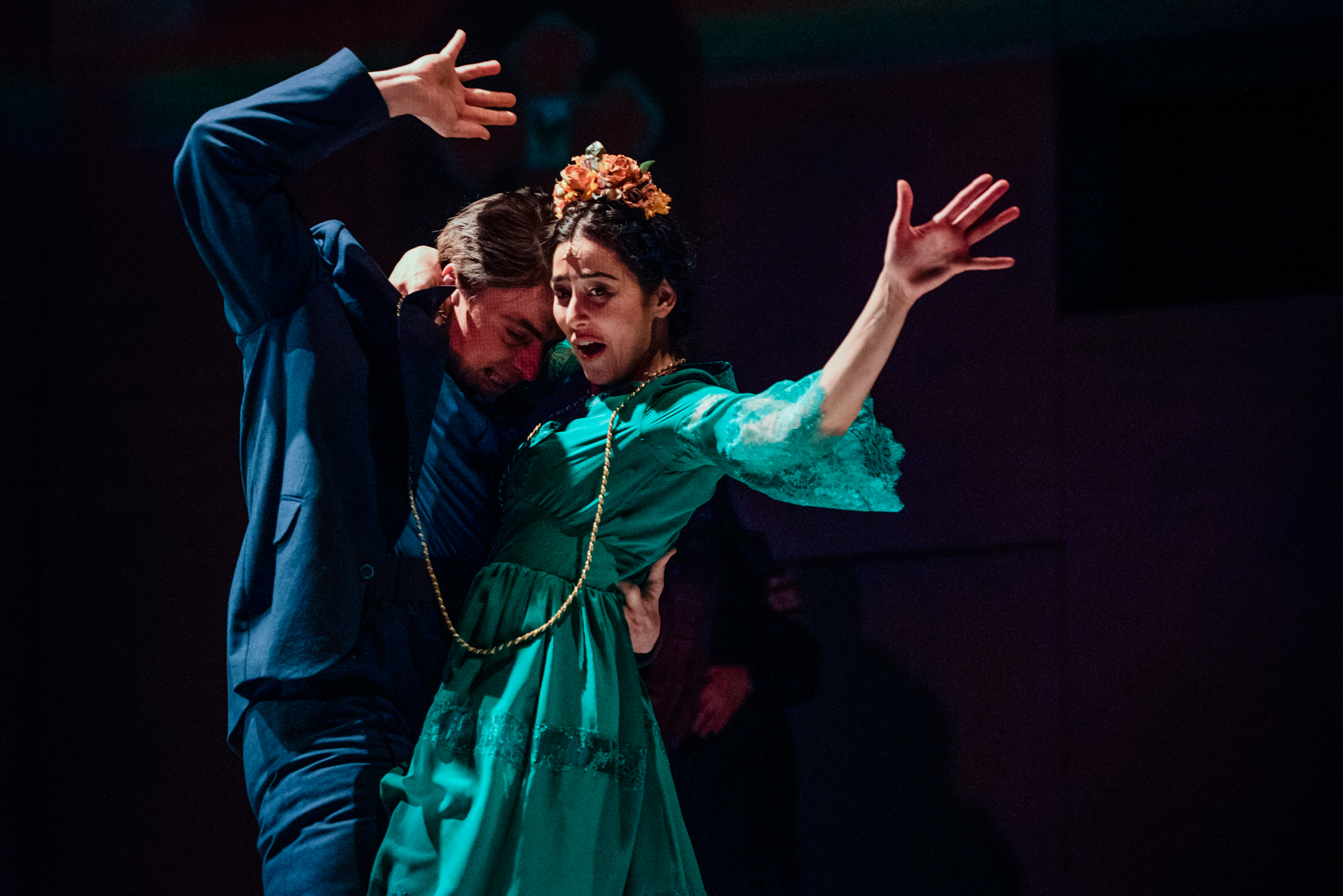 Couple dance closely under colourful stage lighting during Frida Kahlo inspired theatre performance.