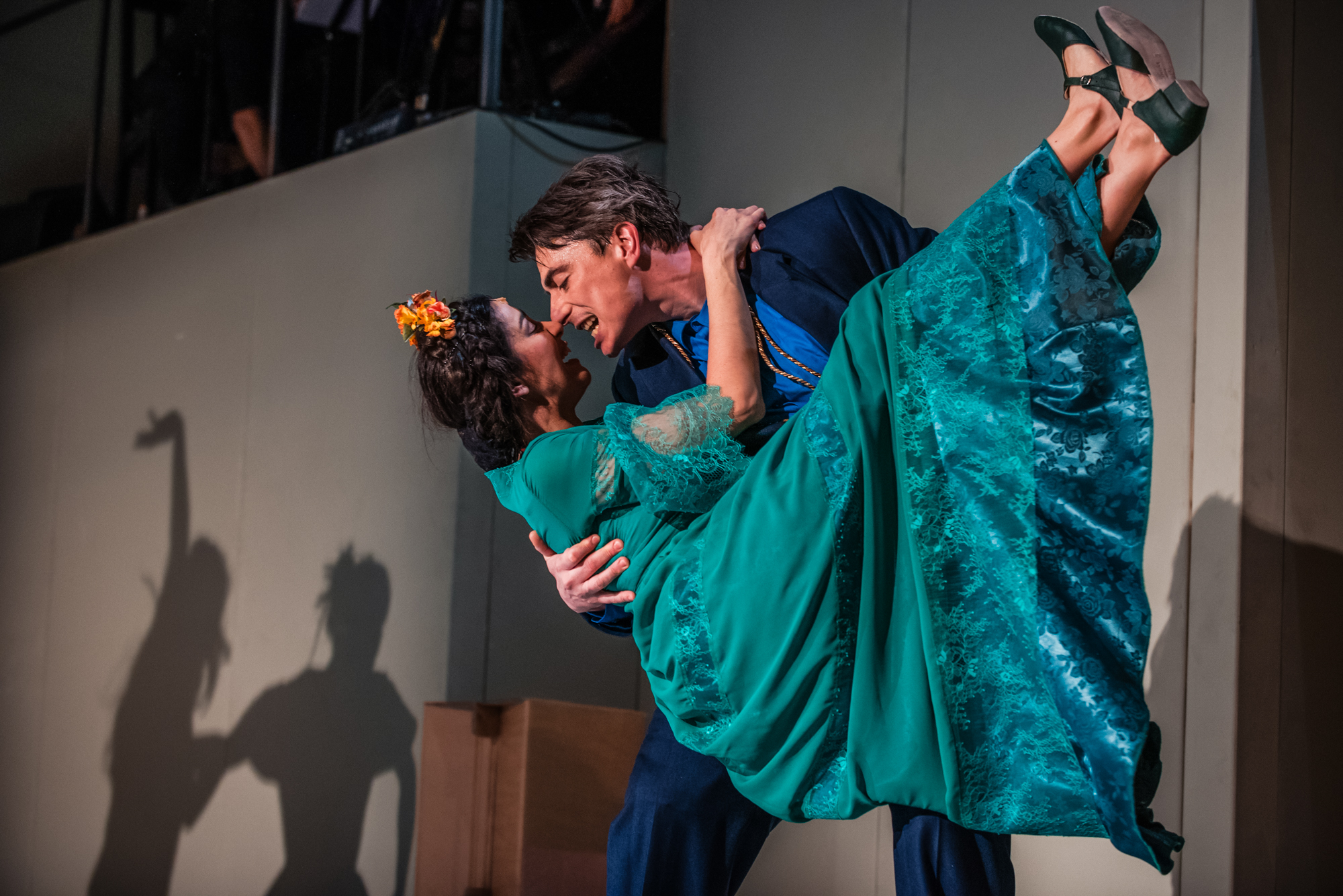 Performer lifts actress in green dress during dramatic dance scene on theatre stage.
