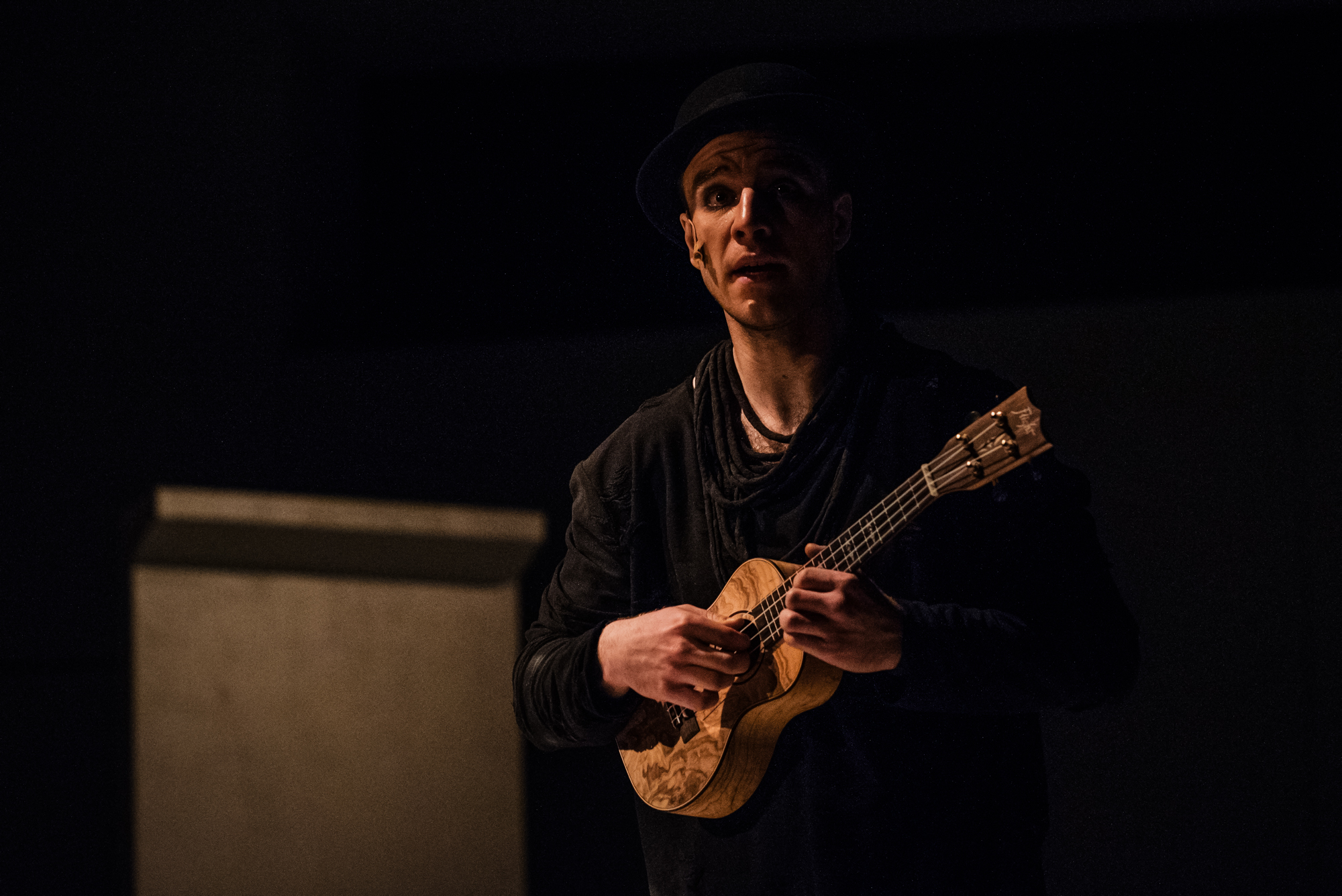 Performer in black costume plays ukulele under low stage lighting during Frida Kahlo theatre production.