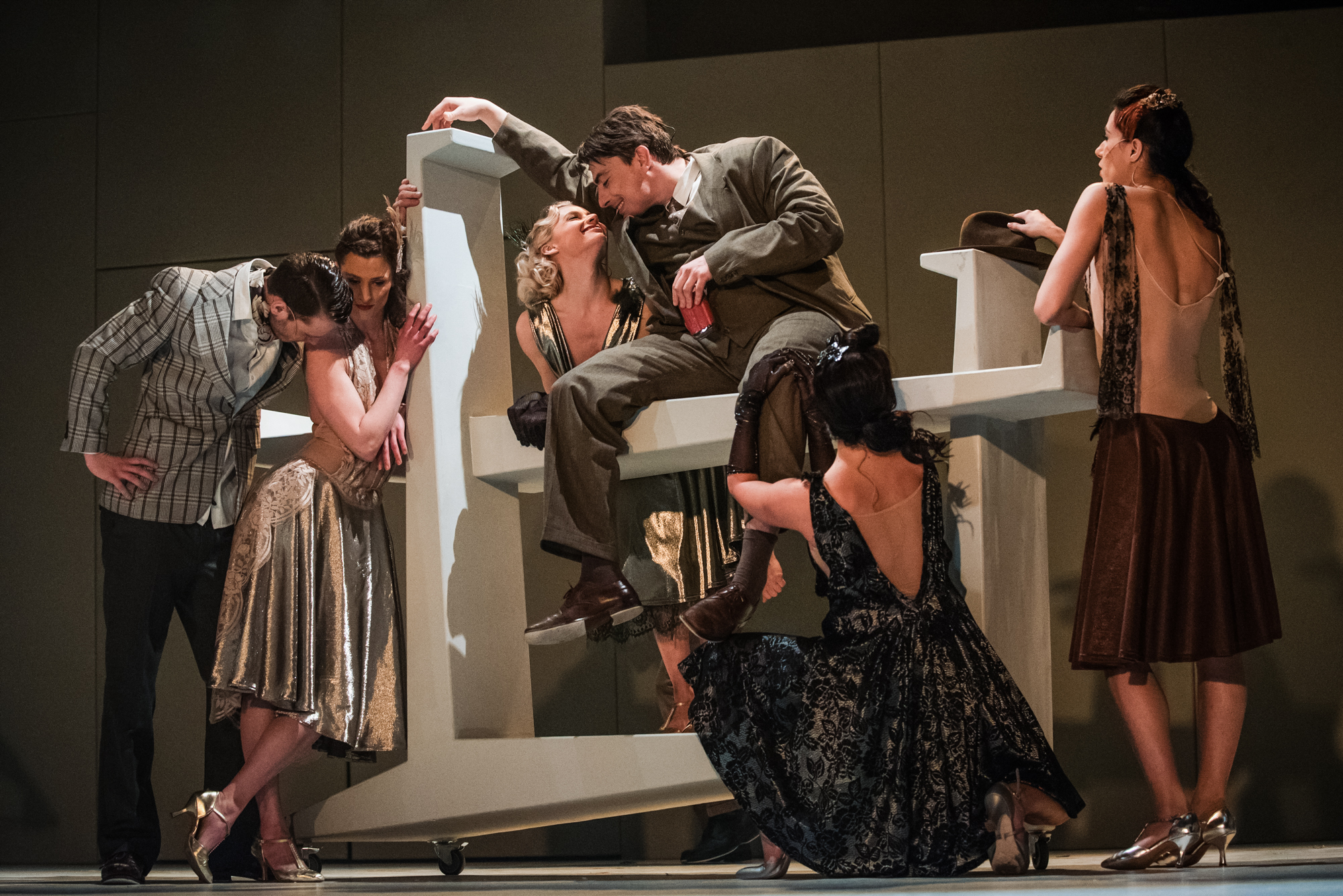 Ensemble cast gather around seated actor on geometric stage set in Frida Kahlo musical.