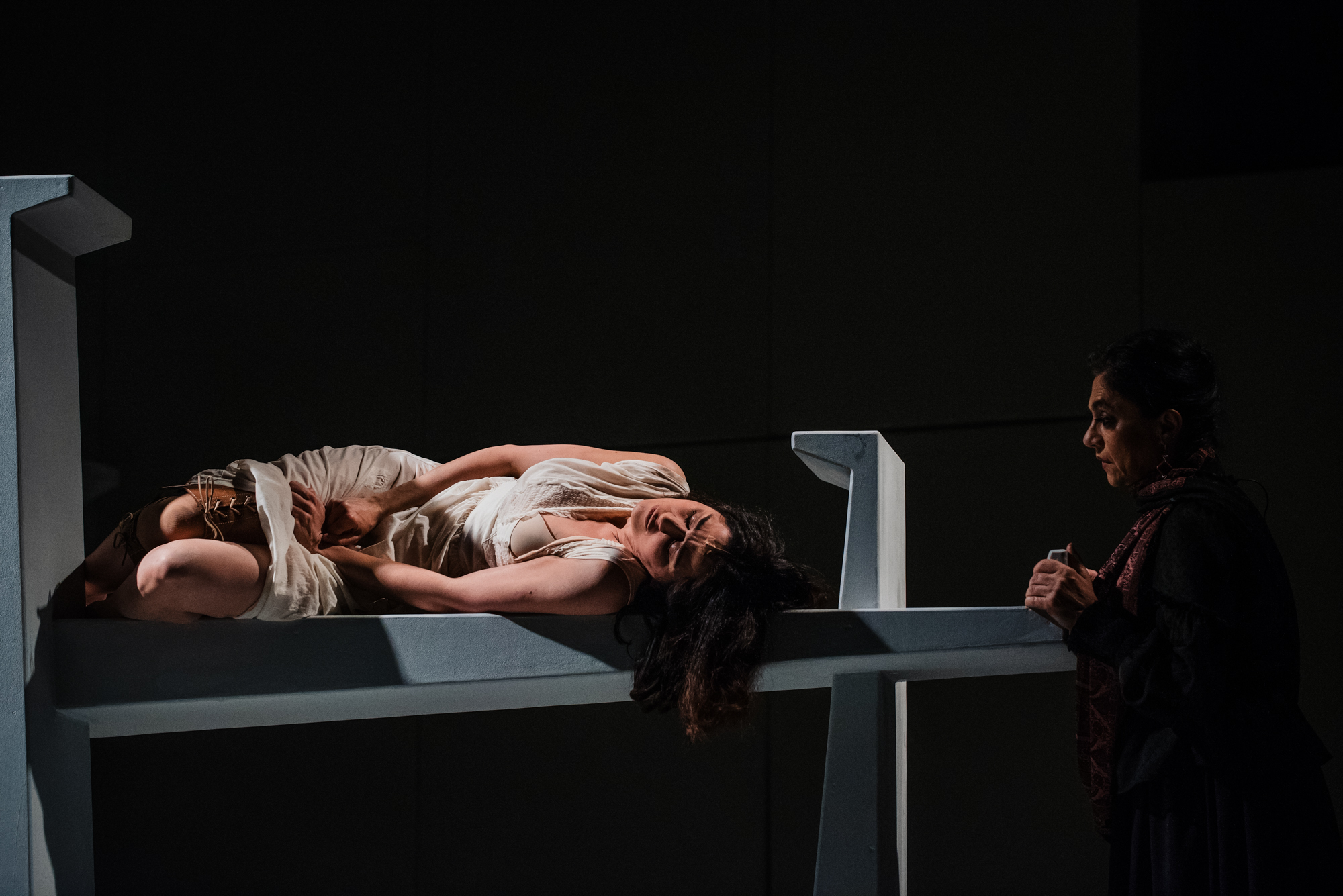 Actress lies curled on white platform during emotional scene in Frida Kahlo theatre production.