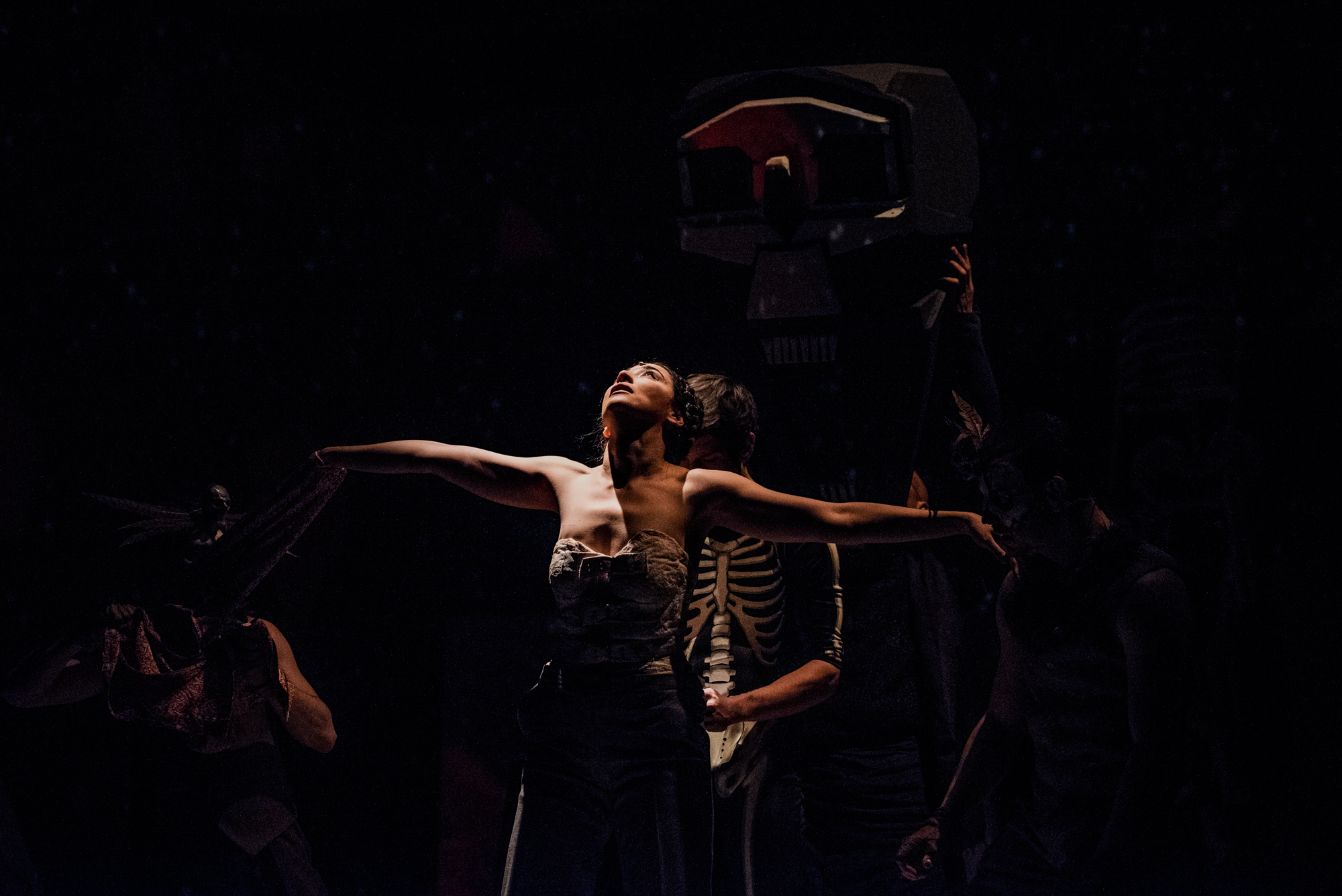 Dancer reaches upward in dramatic low-light scene during Frida Kahlo inspired theatre performance.