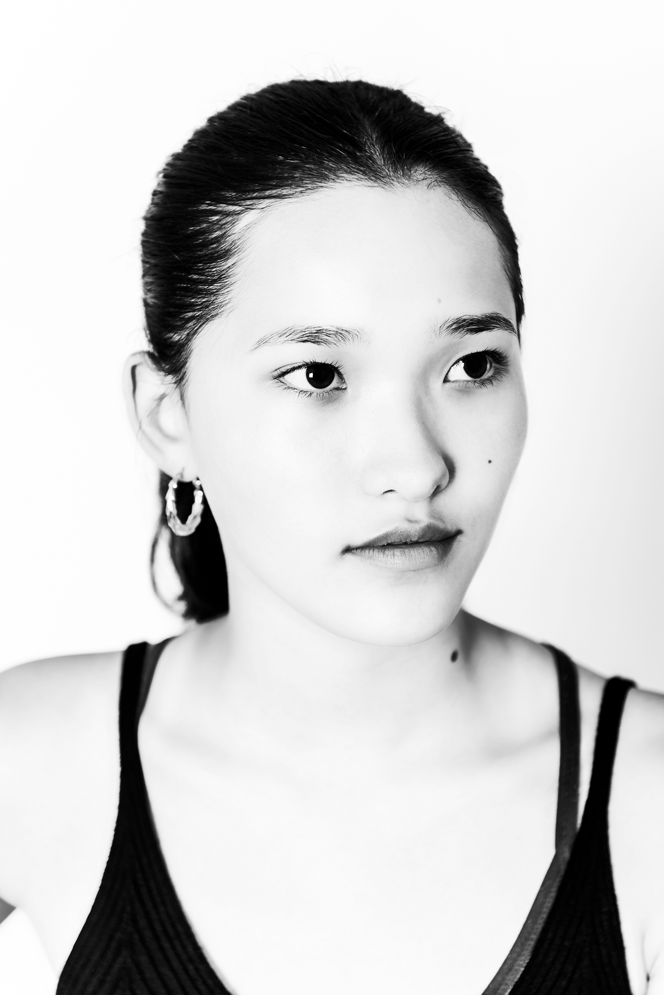Black and white beauty portrait with slicked-back ponytail and soft editorial expression.