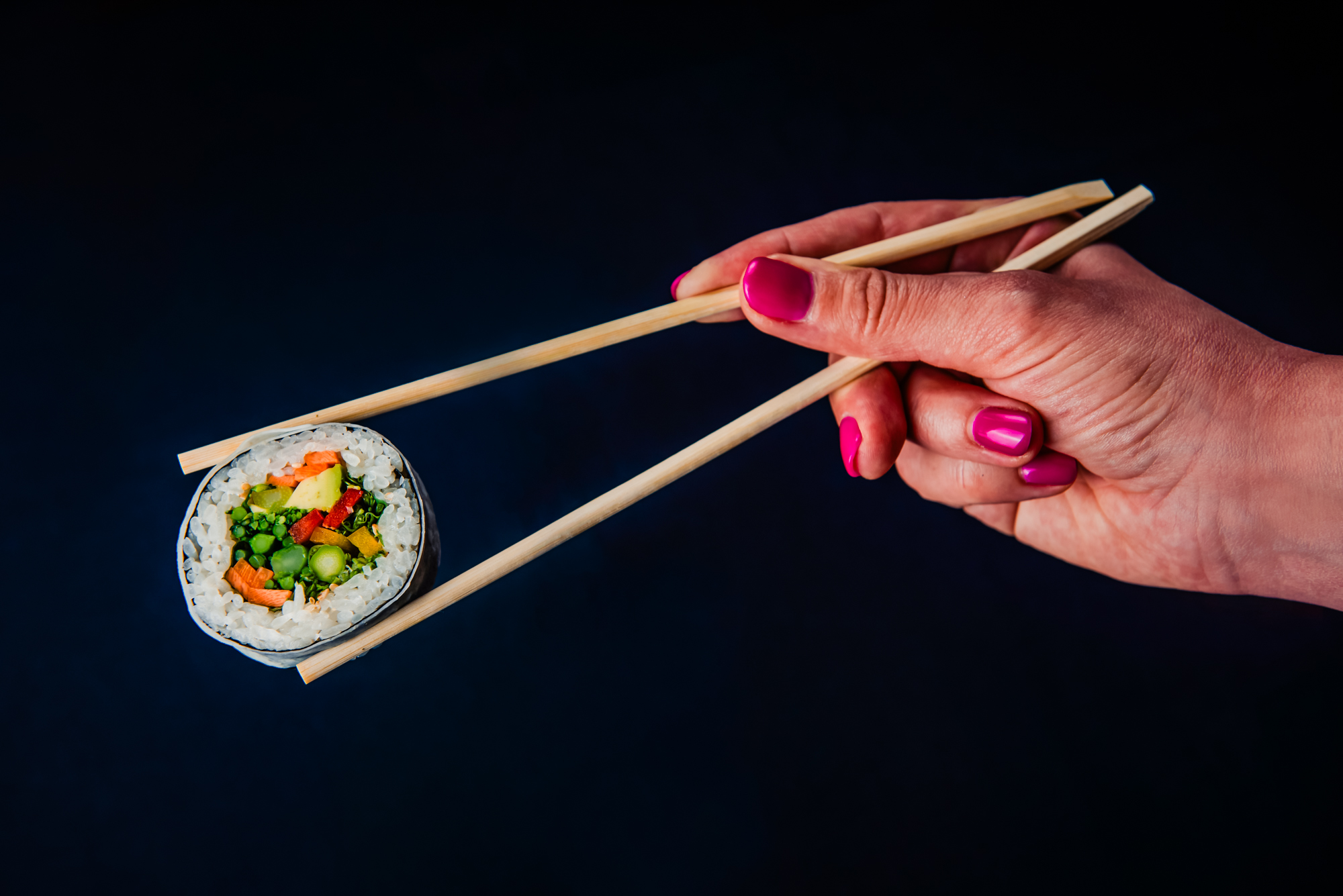 Hand holding chopsticks with a colourful vegetable sushi roll suspended in mid-air at Nobu Budapest.