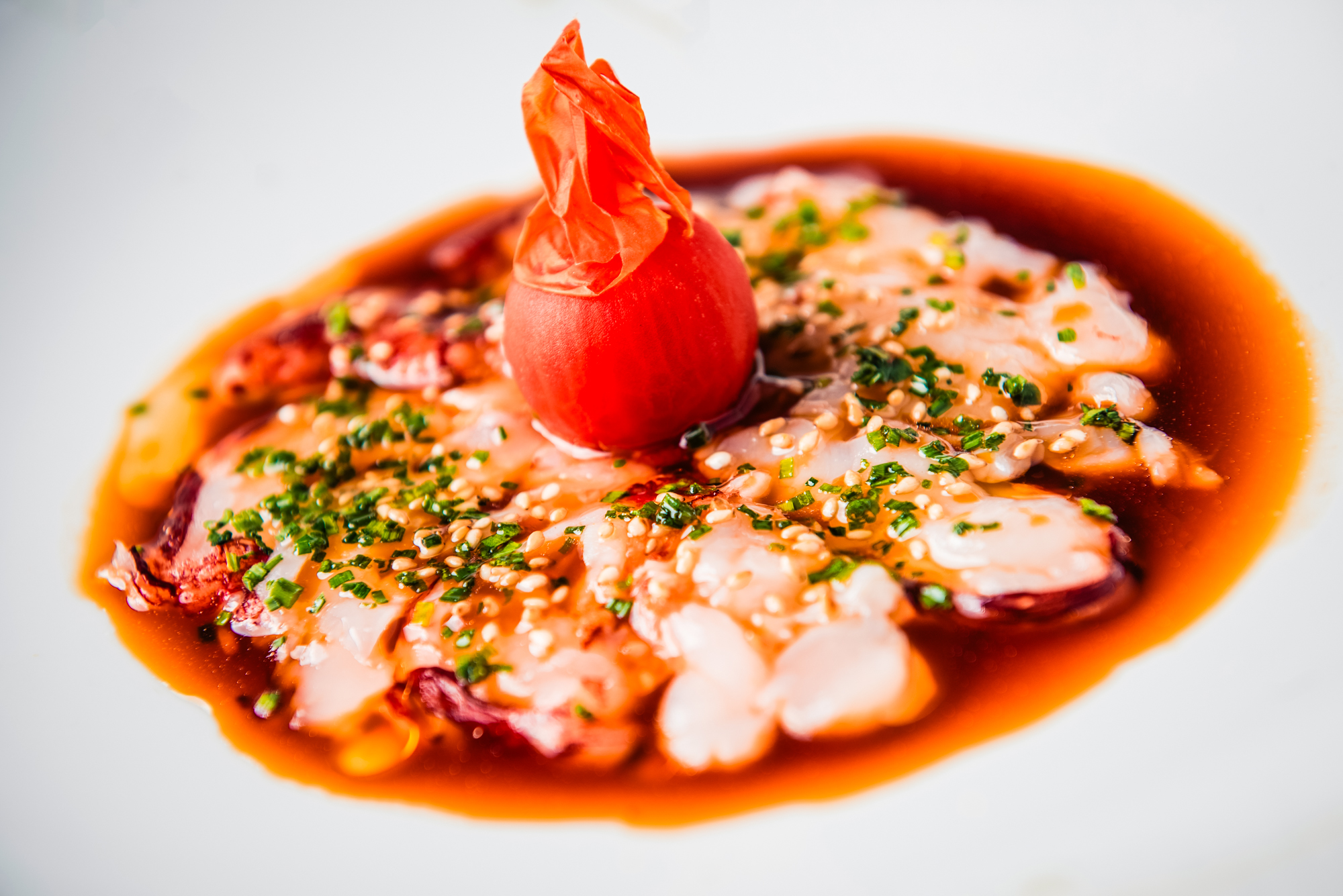 Octopus carpaccio served in a rich sauce with sesame seeds and a pickled garnish at Nobu Budapest.