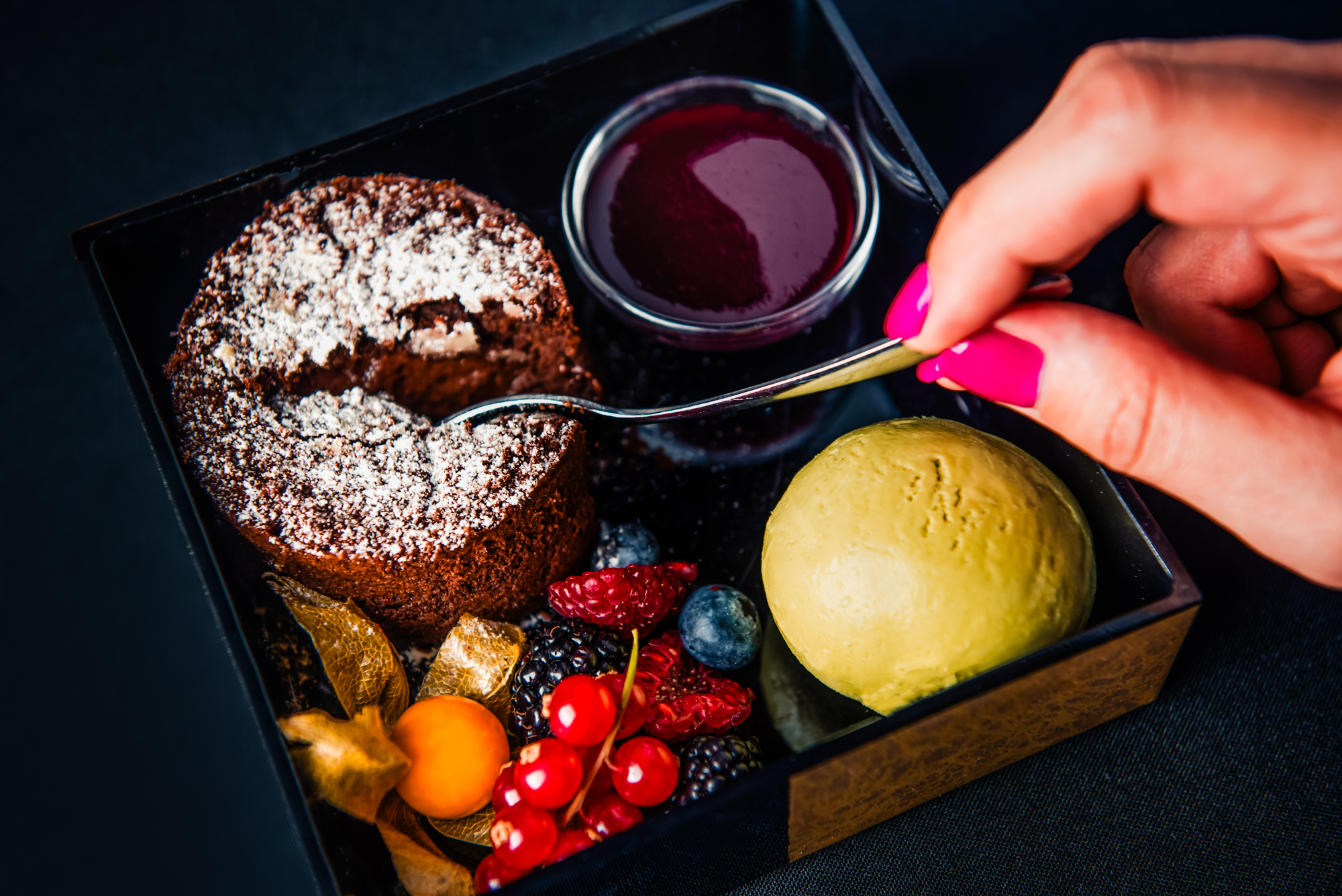 Spoon breaking into warm chocolate fondant served with berry coulis, sorbet, and fresh berries.