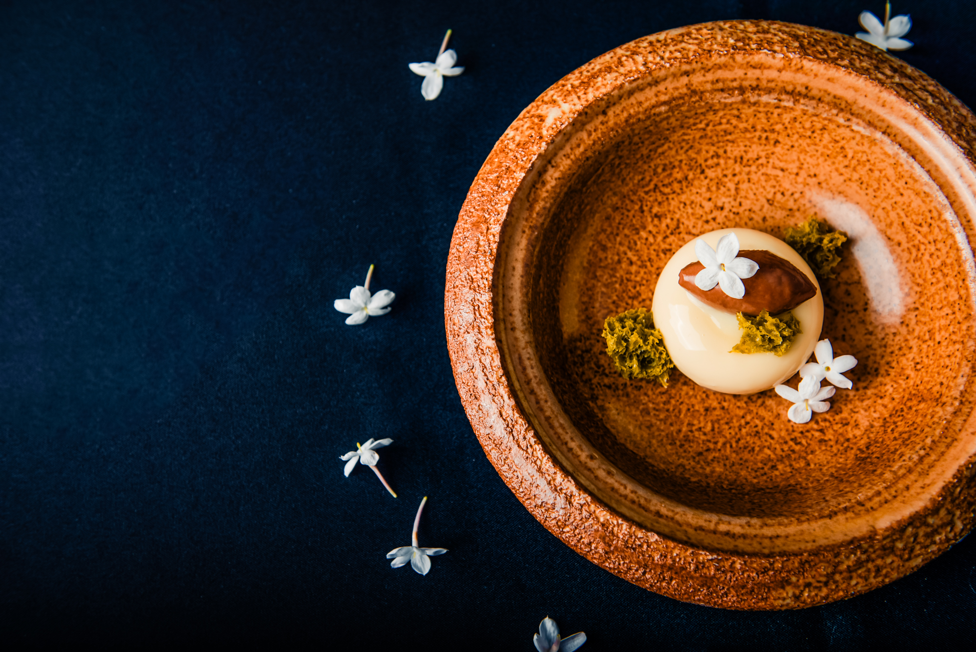 Delicate white chocolate dessert presented in a rustic ceramic bowl with edible flowers at Nobu Budapest restaurant.