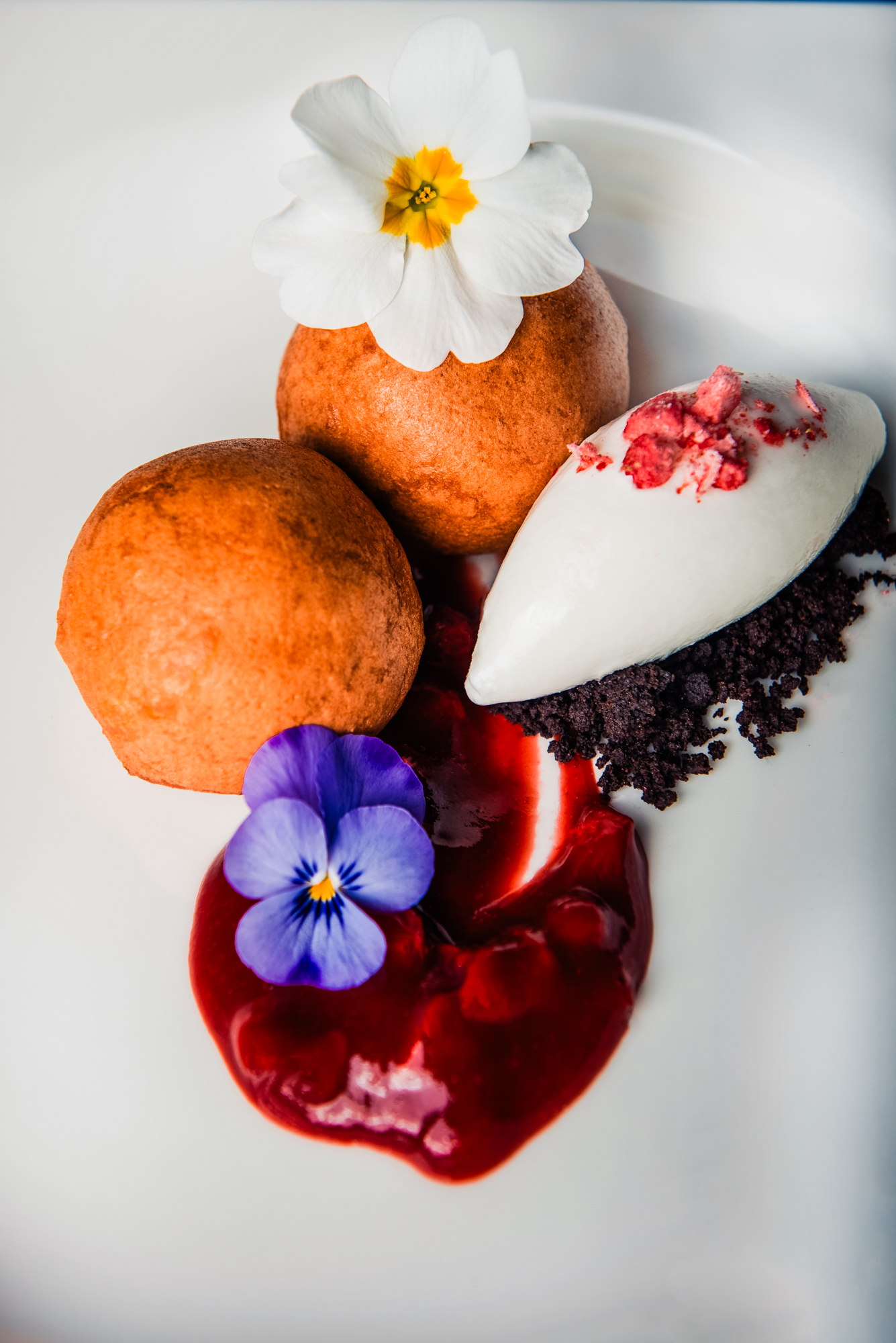Chocolate truffles with berry sauce, vanilla quenelle, and edible flowers on a white plate.