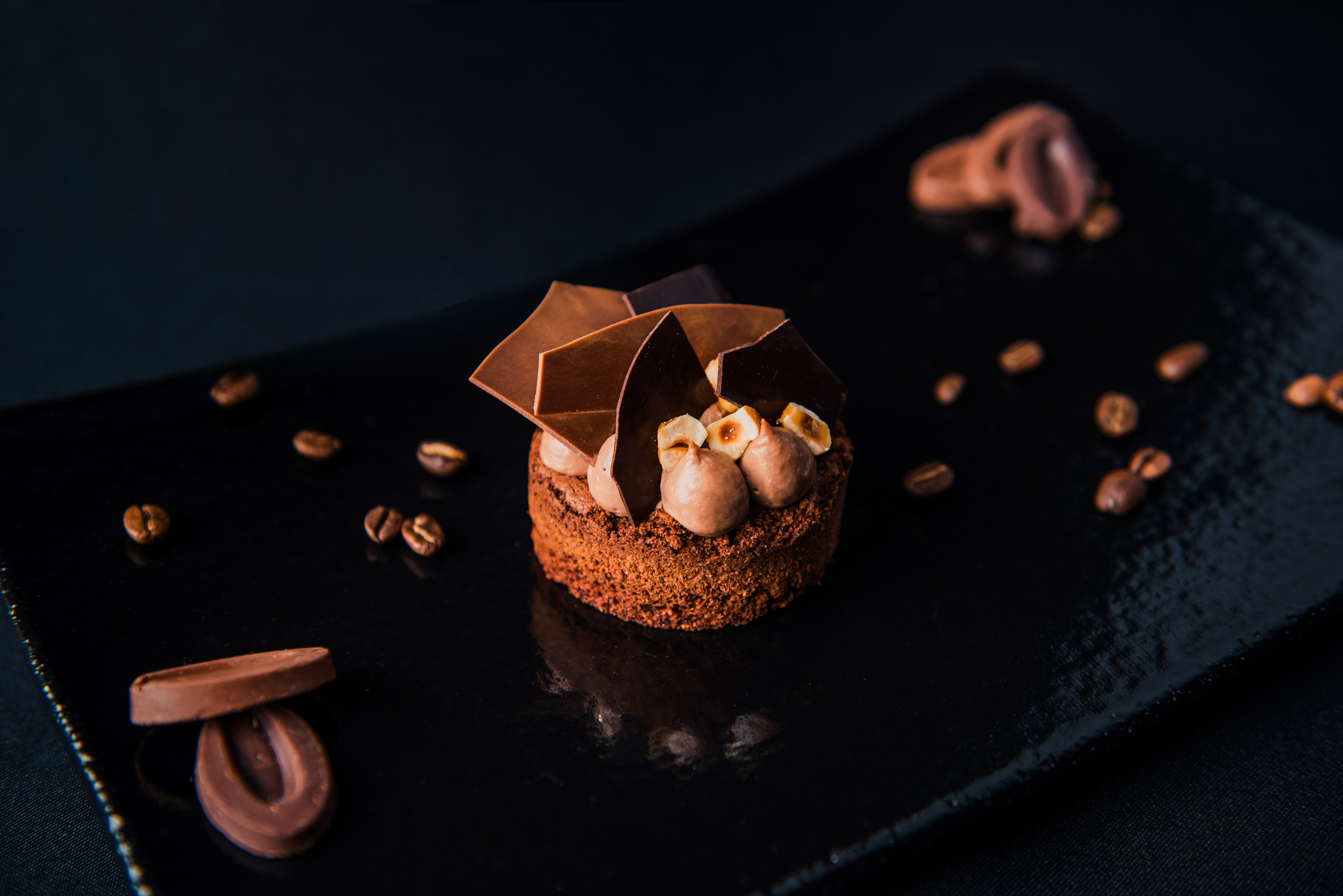Chocolate tart topped with chocolate shards, mousse, and roasted hazelnuts.