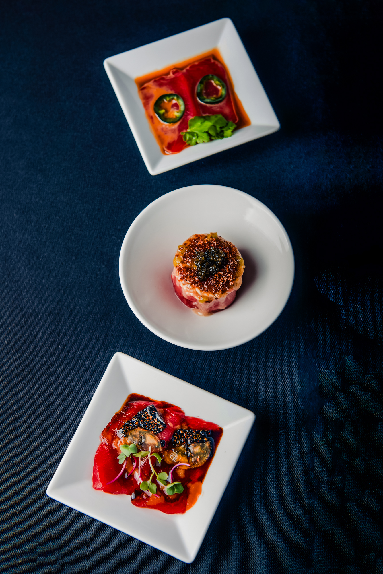 Japanese tasting menu trio presented on white plates against a dark background at Nobu Budapest.