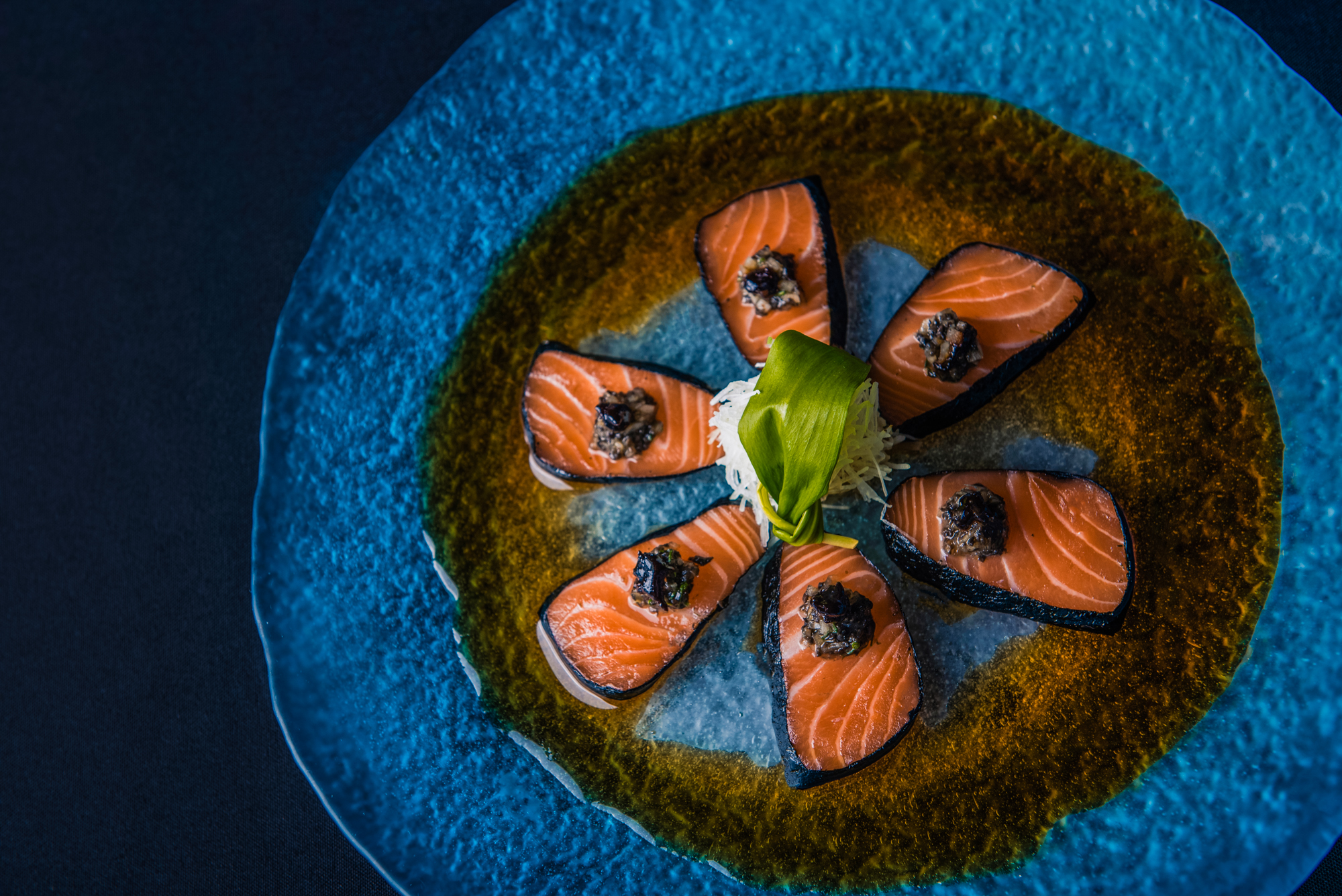 Salmon sashimi slices arranged in a flower pattern on a textured blue plate at Nobu Budapest restaurant.