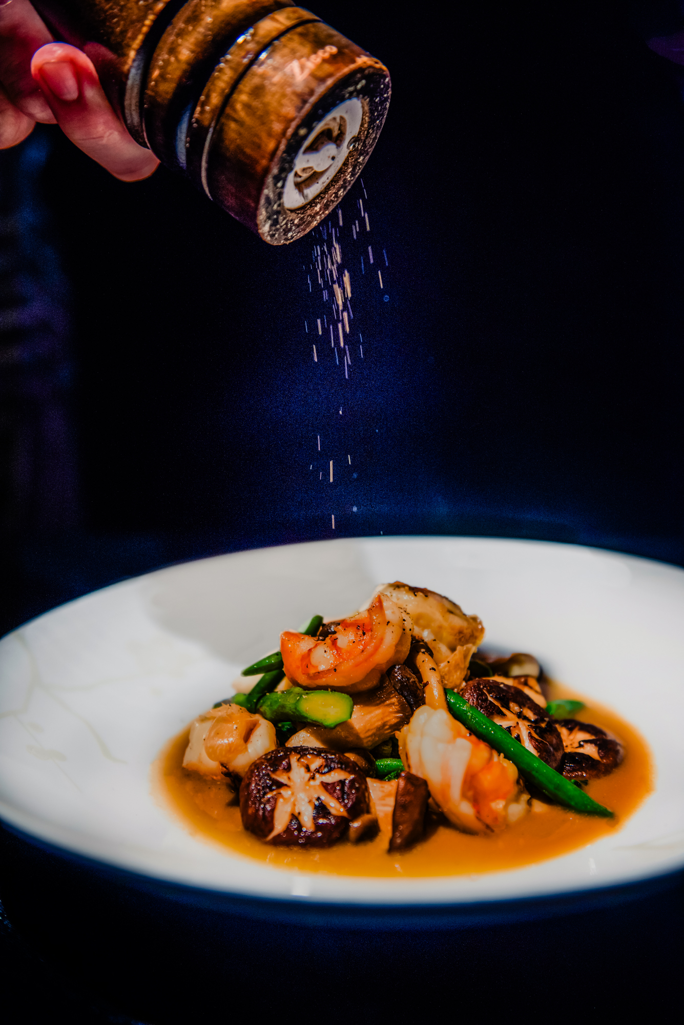 Freshly ground pepper falling onto a seafood dish with mushrooms and green vegetables at Nobu Budapest restaurant.