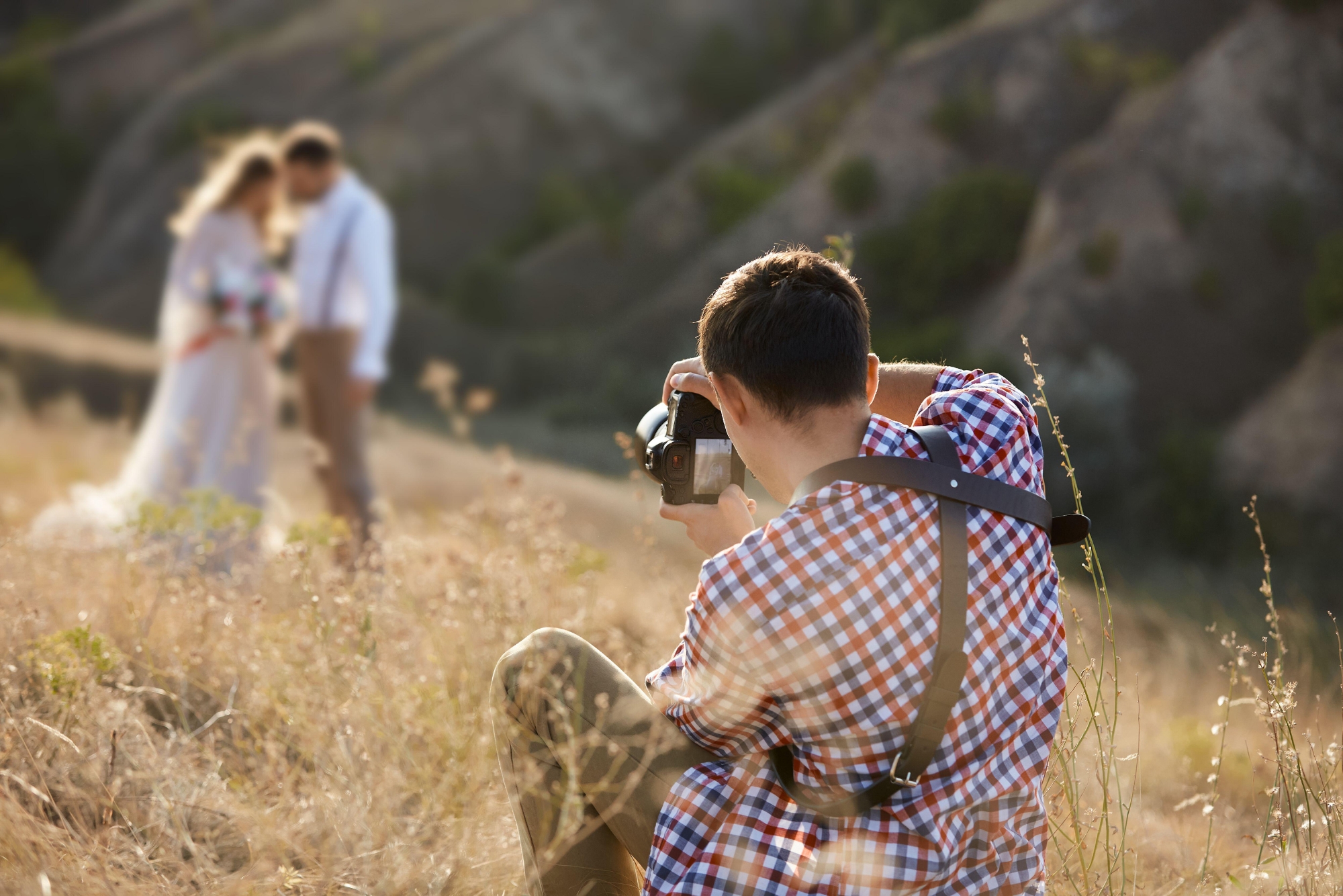 A man is taking portraits of a couple in a natural landscape during golden hour light.