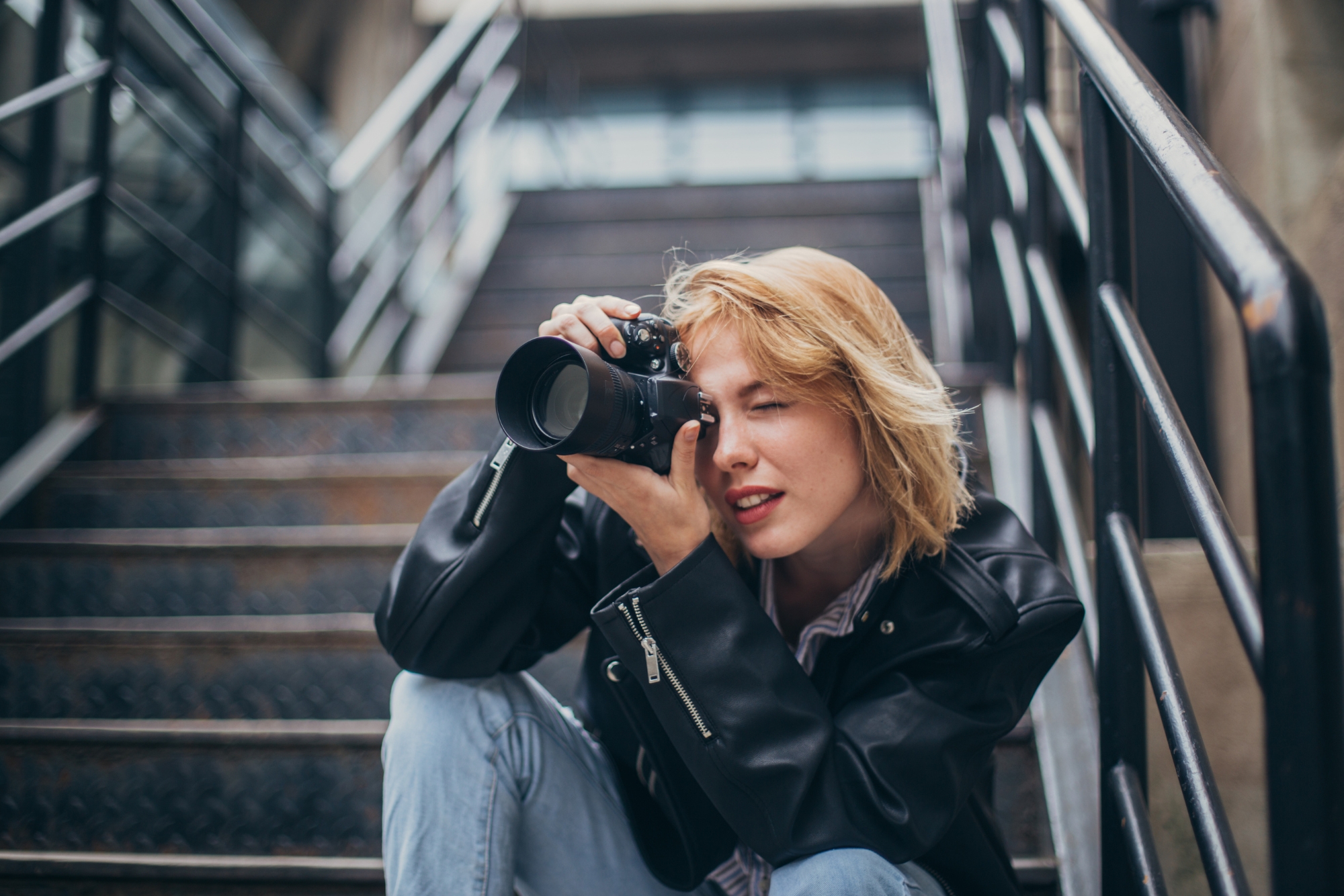 A woman sitting on stairs taking a photo, showing a quiet and focused shooting moment.