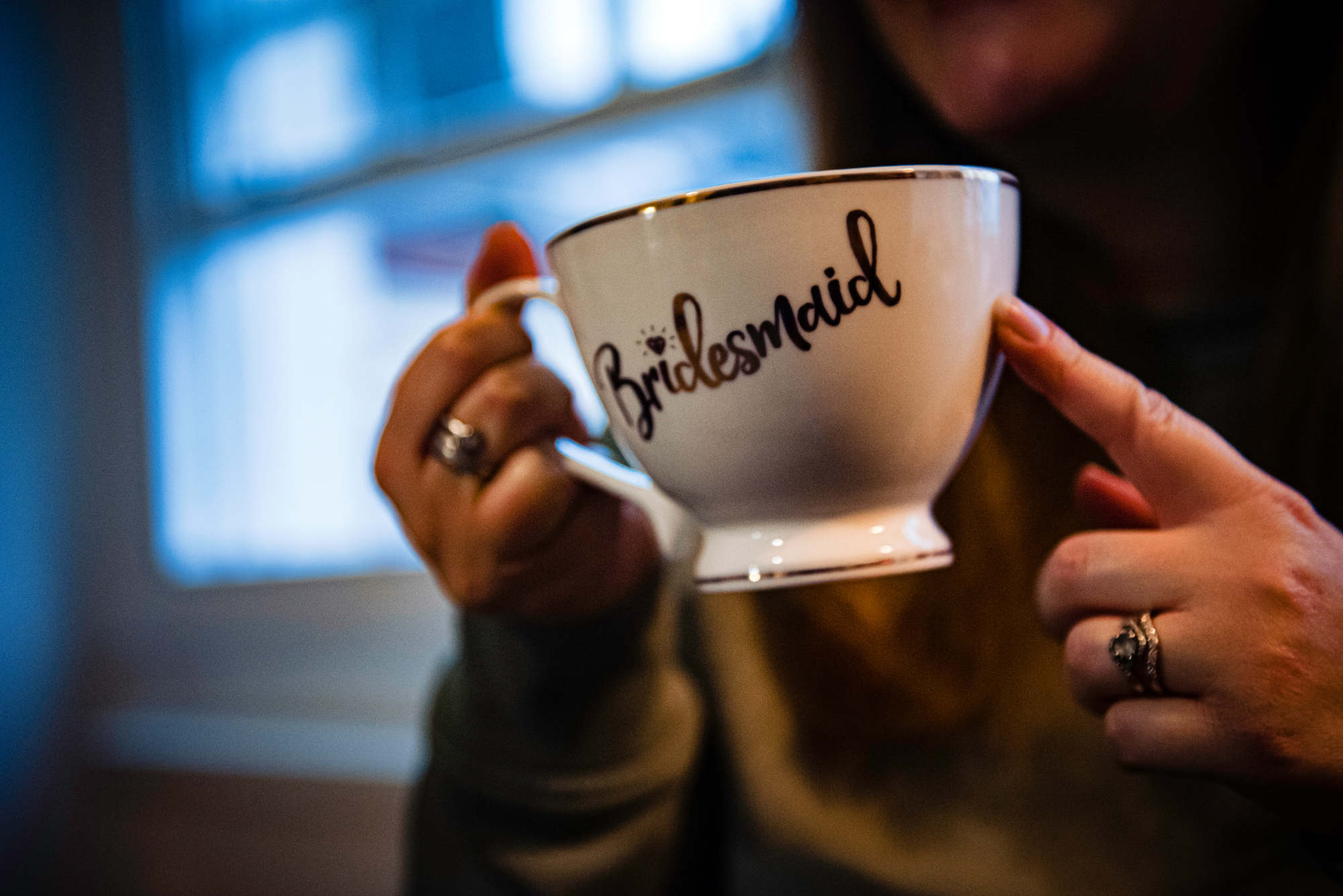 Bridesmaid holding a white mug with ‘Bridesmaid’ lettering and smiling behind it.
