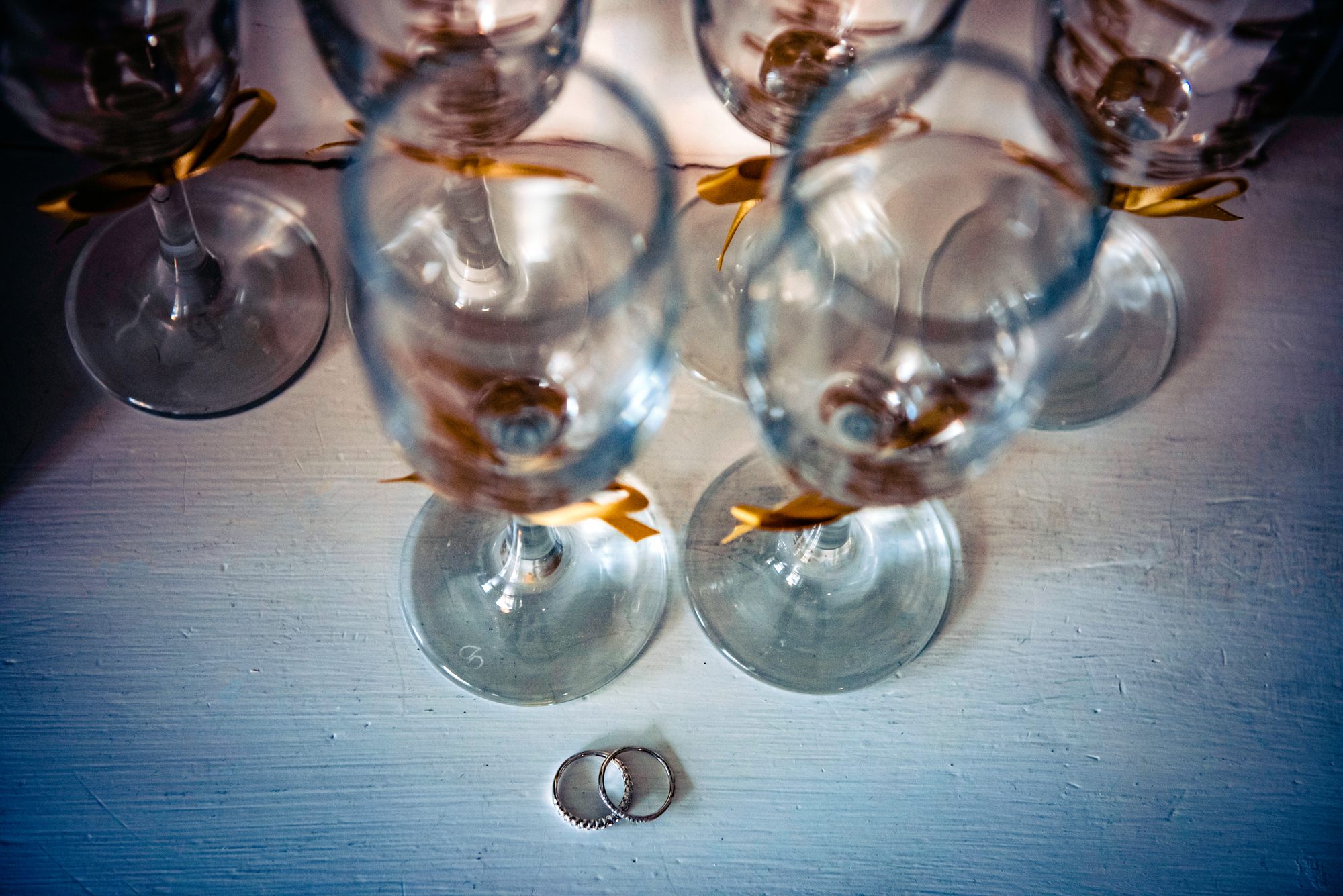 Wedding rings resting beside champagne glasses with gold ribbons on a white table.