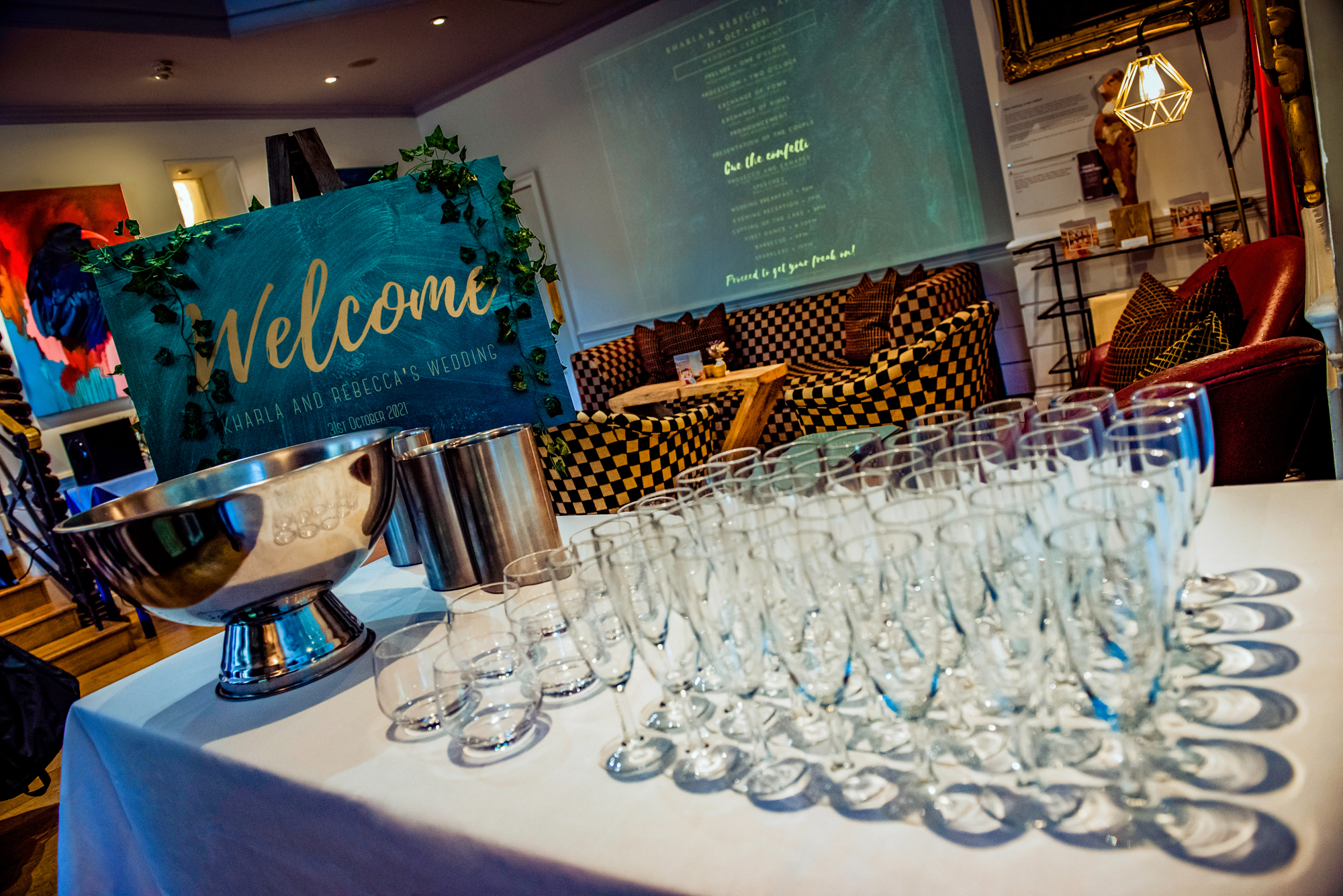 Wedding welcome table at The Square Club Bristol with teal sign, champagne glasses, and ivy decor.