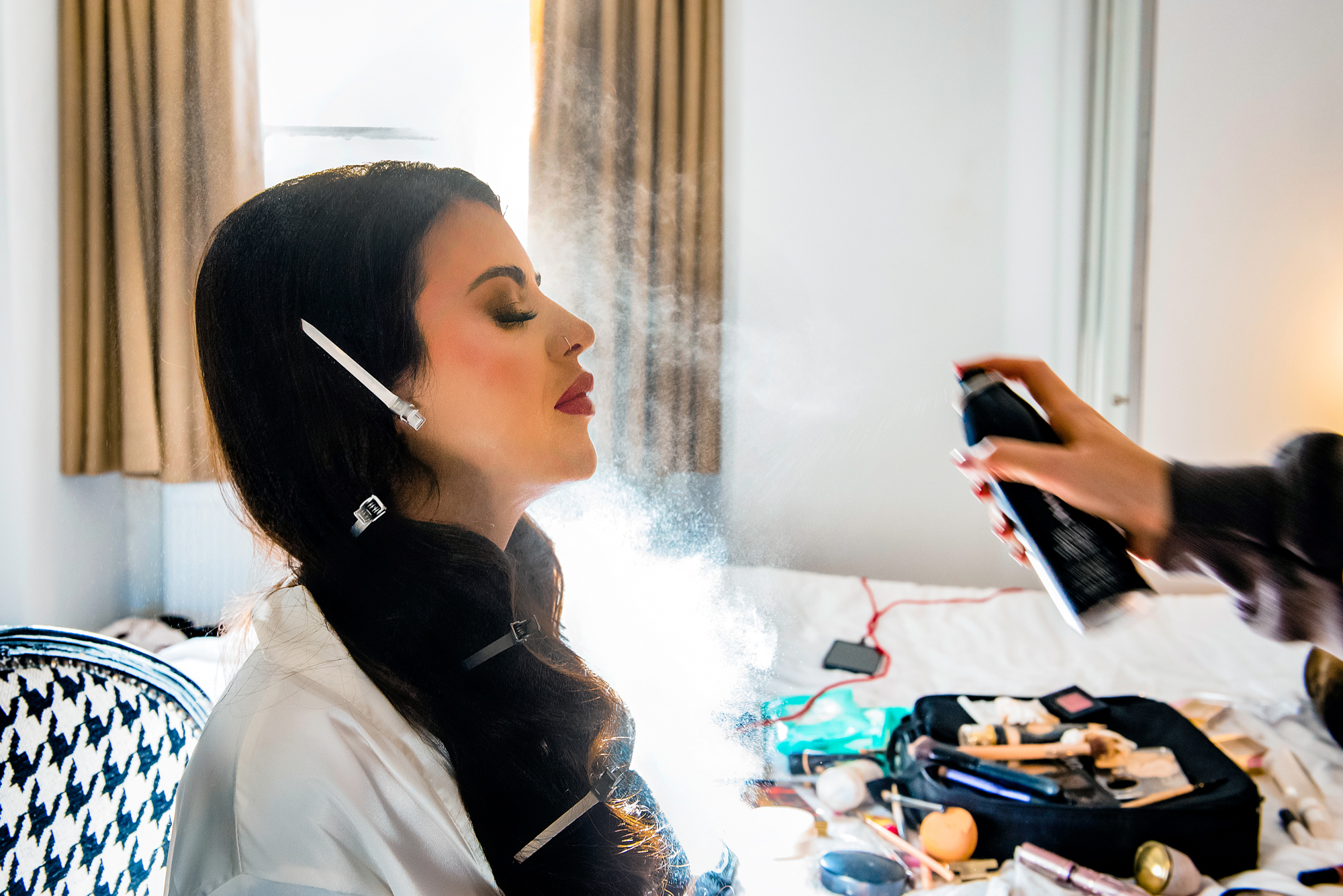 Bride having hairspray applied while getting ready, golden light illuminating the mist in the air.