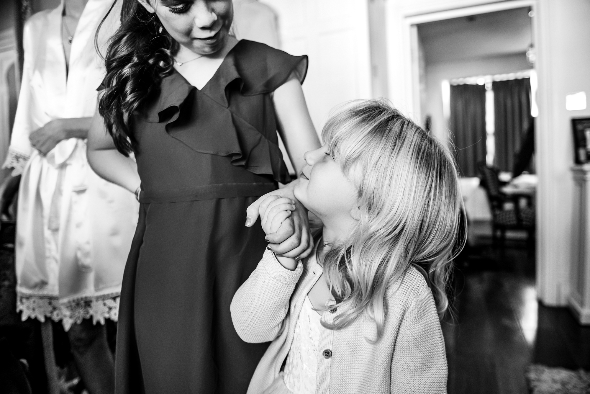 Two young girls holding hands and smiling at each other during wedding morning preparations.