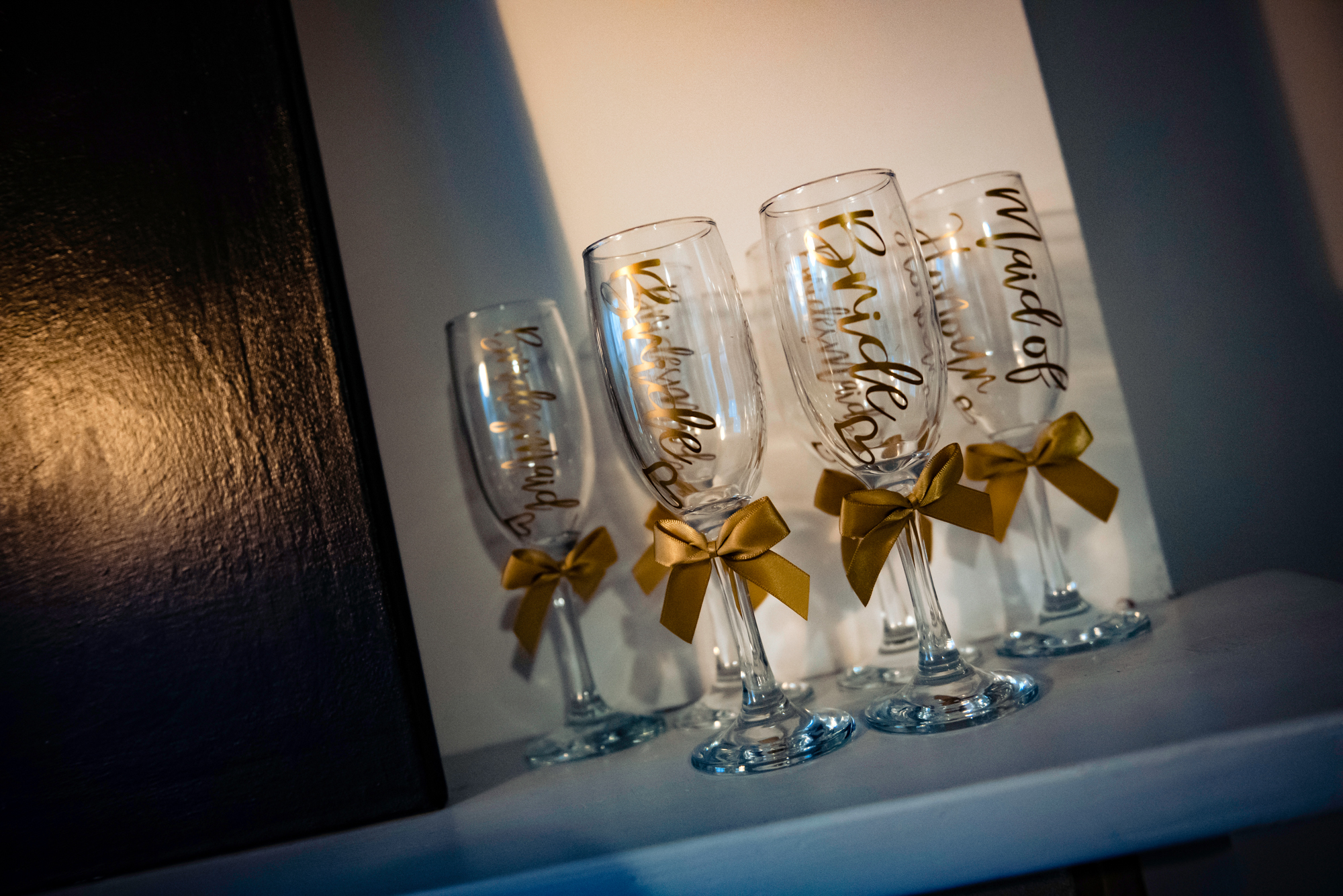 Personalised champagne flutes with gold bows lined up on a shelf before the ceremony.