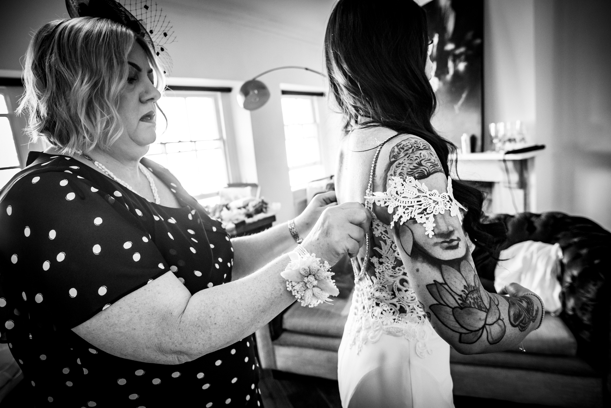 Mother of the bride fastening lace buttons on daughter’s wedding dress.