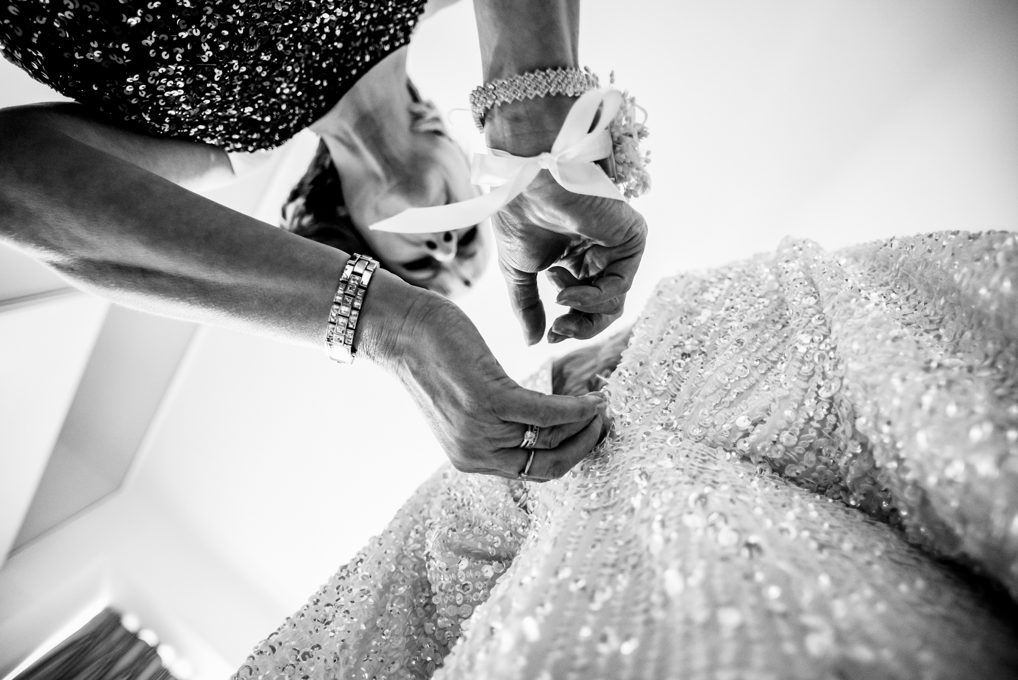 Mother fastening the back of a sequinned wedding dress in morning light before the ceremony.