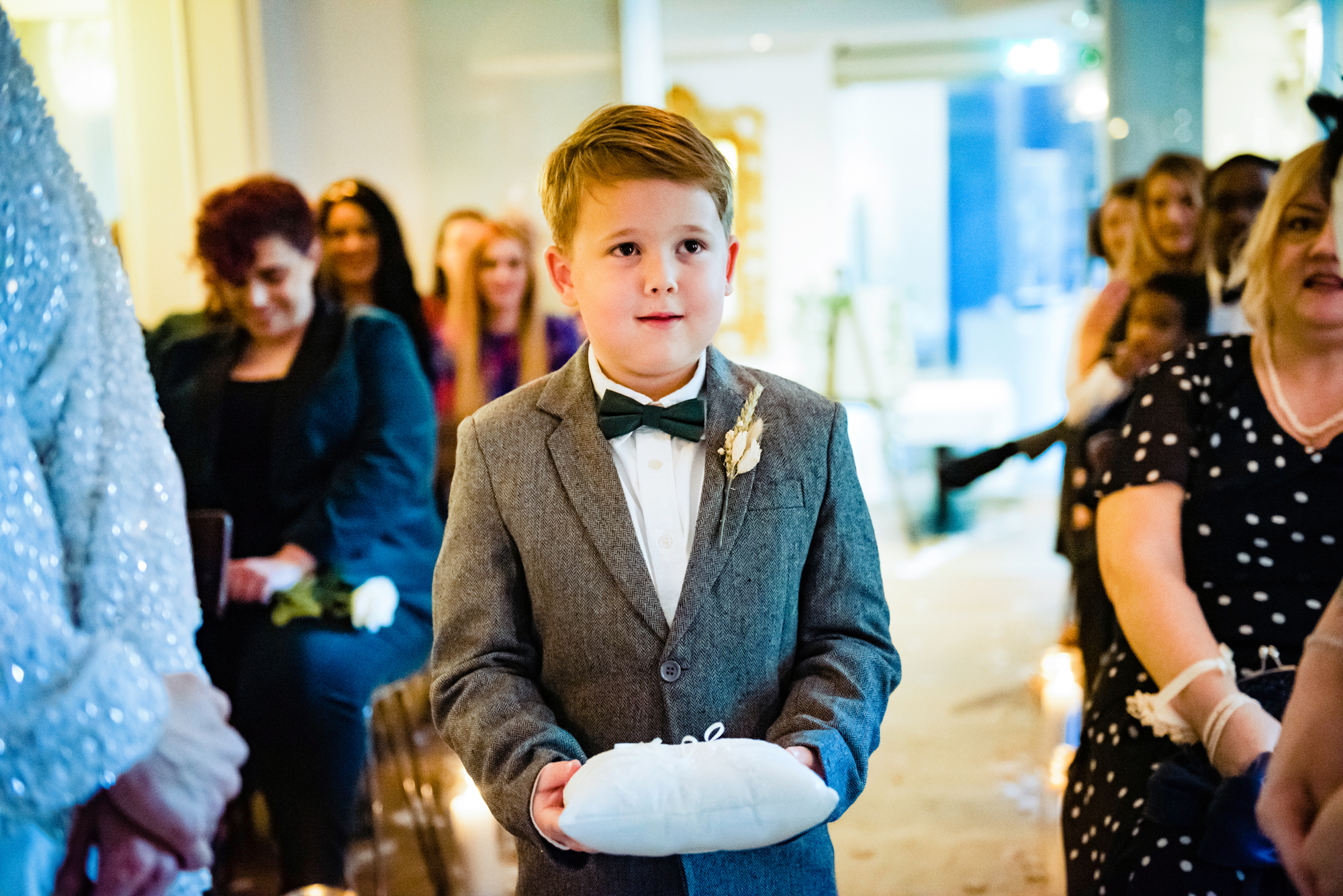 Young ring bearer walking down the aisle holding a small white pillow with wedding rings.