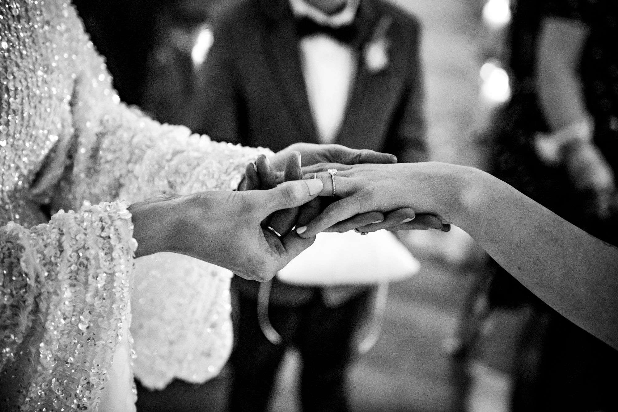 Exchange of rings captured in black and white, showing hands gently intertwined.