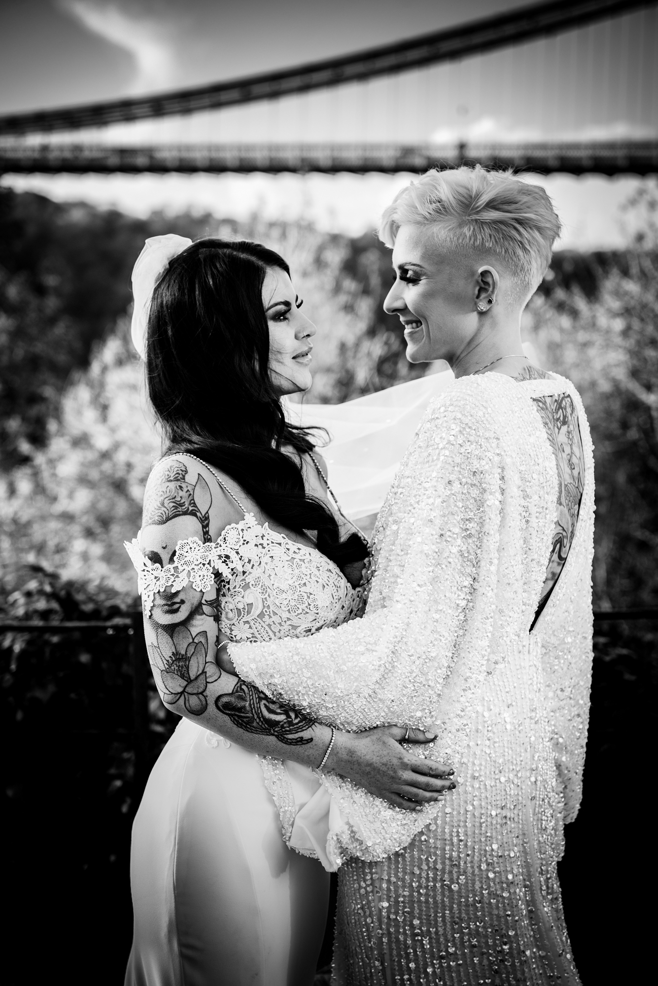 Brides smiling at each other, with the bridge in the distance.