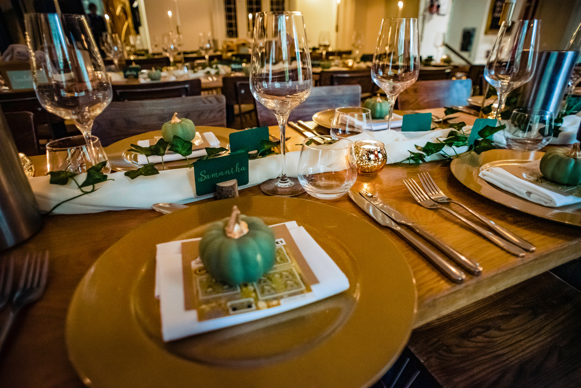Close-up of wedding table place setting with gold plates, name cards, and green pumpkin décor.