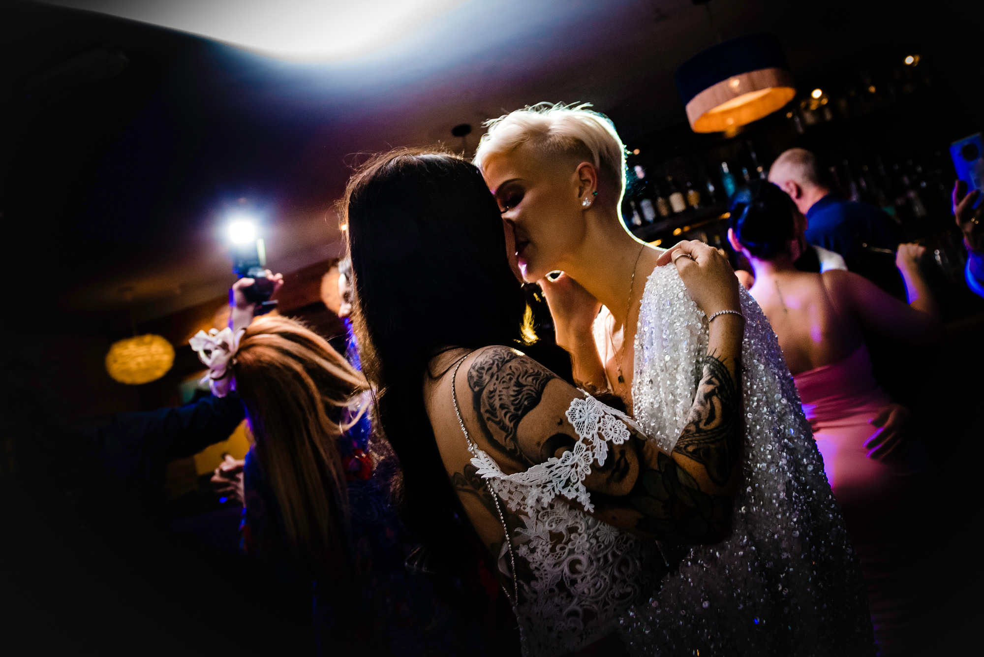 Close-up of brides sharing a kiss on the dance floor under colourful evening lights.