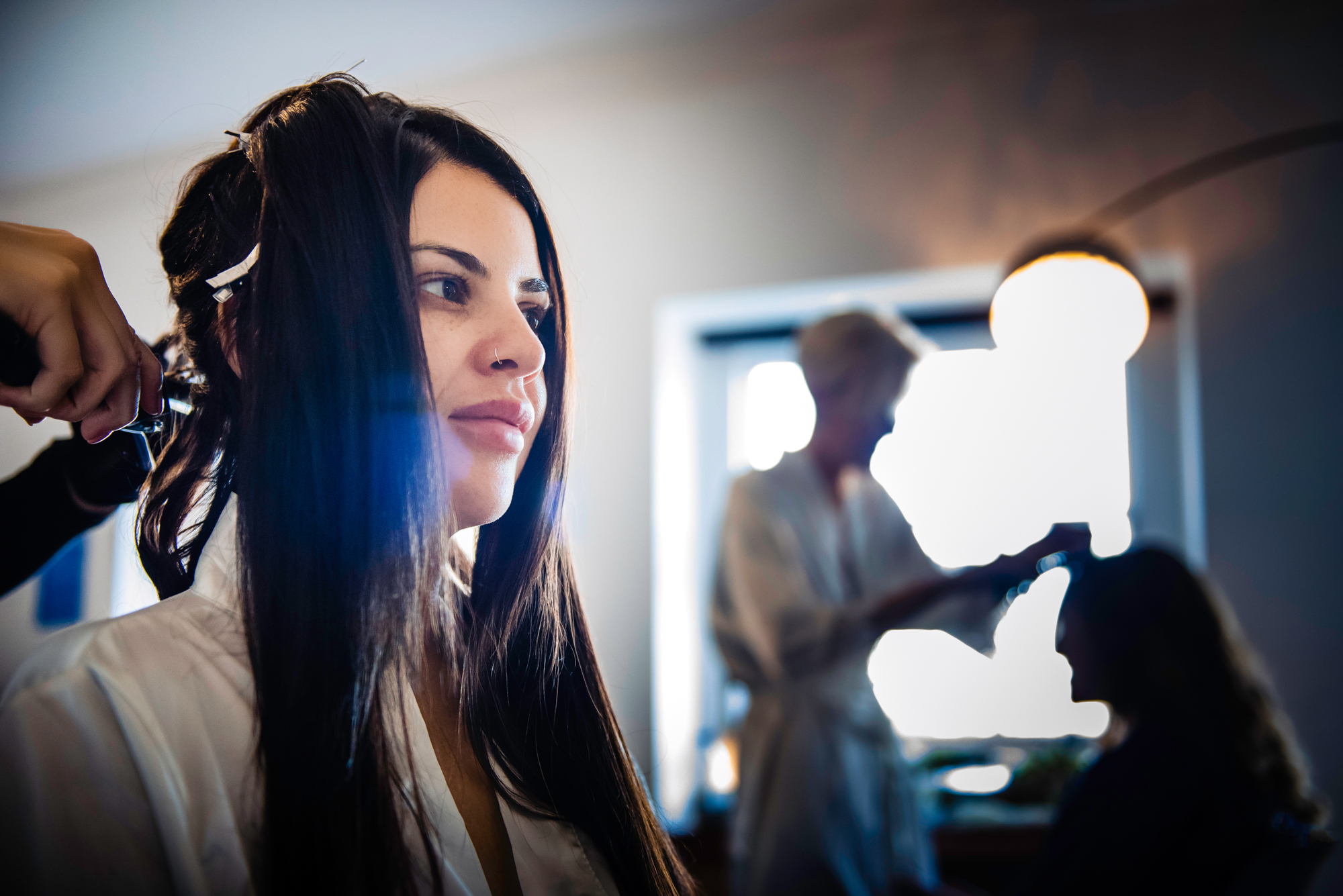 Bride with long dark hair having curls styled during relaxed morning preparations.