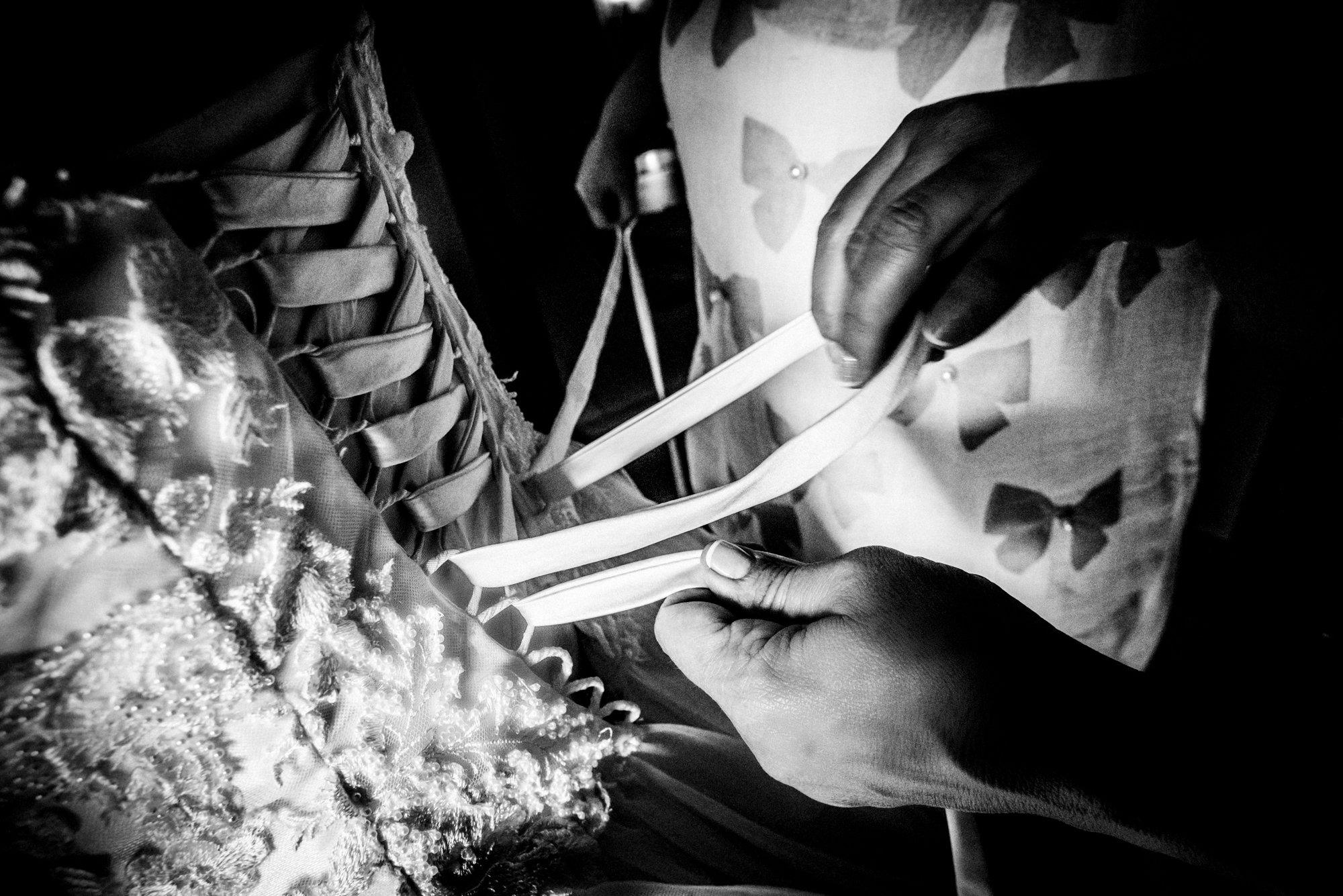Close-up black and white photo of hands tightening the lace back of a wedding dress.