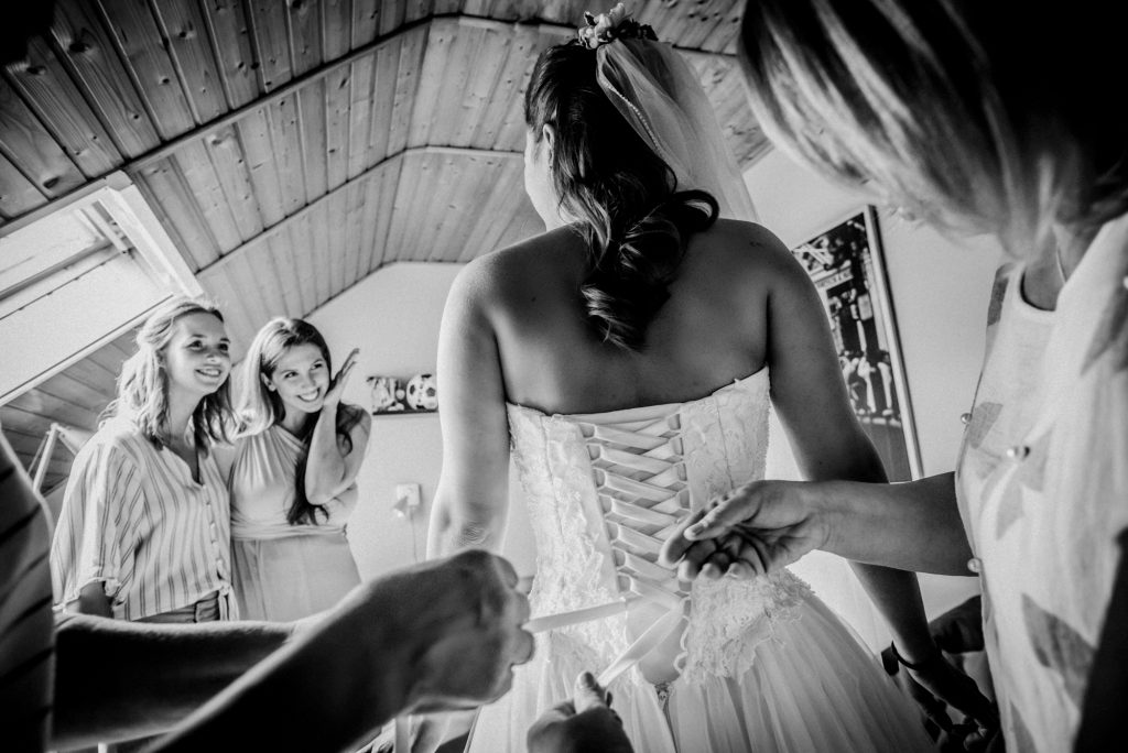 Bridesmaids watching as the bride’s corset wedding dress is tied before the ceremony.